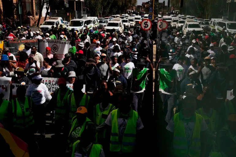محتجون في شوارع جوهانسبرغ يرتدون زيّاً موحداً، يحملون لافتات ويعبرون عن مطالبهم، وسط أجواء من التوتر والاحتجاجات.