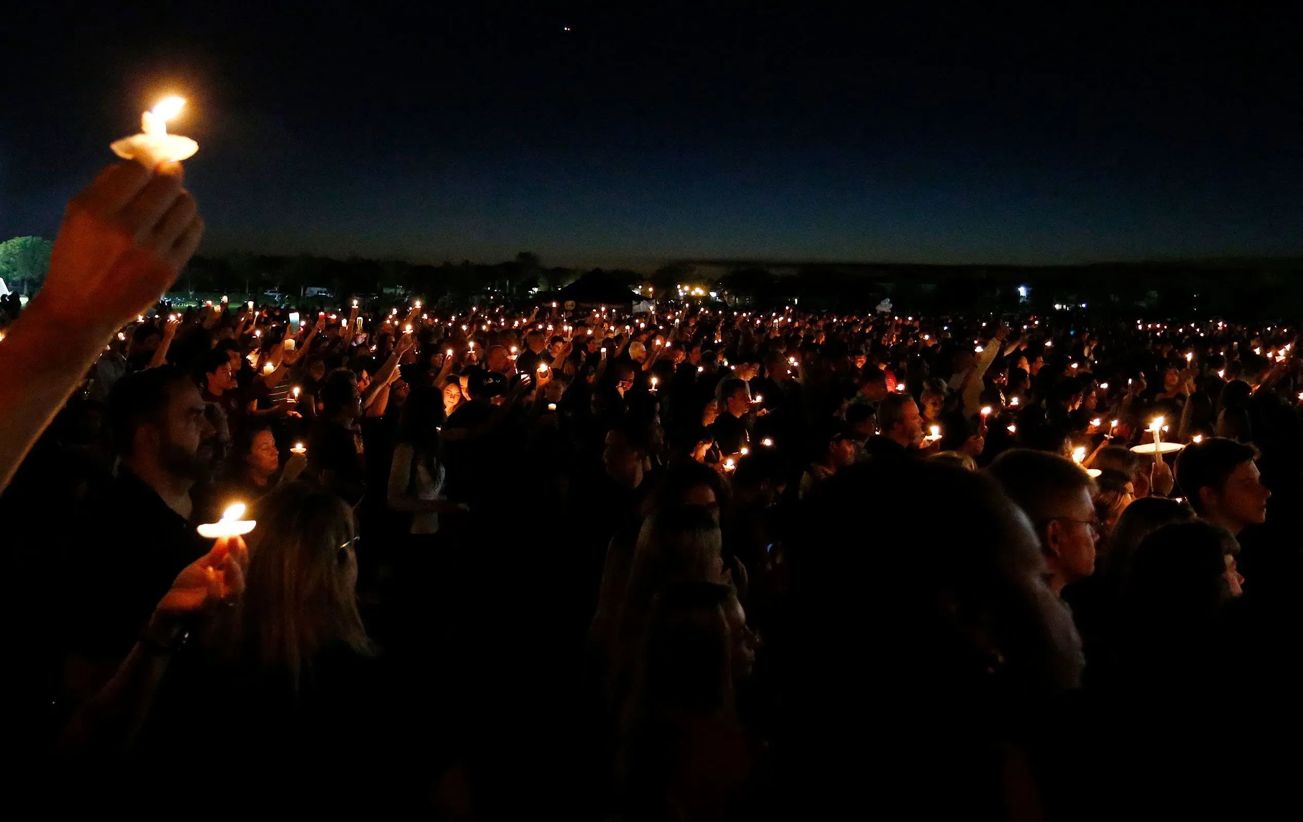 تجمع حشود كبيرة في ليلة مظلمة، يحملون الشموع المضيئة في إحياء ذكرى ضحايا حوادث إطلاق النار في المدارس، مما يعكس التضامن والمطالبة بالمساءلة.