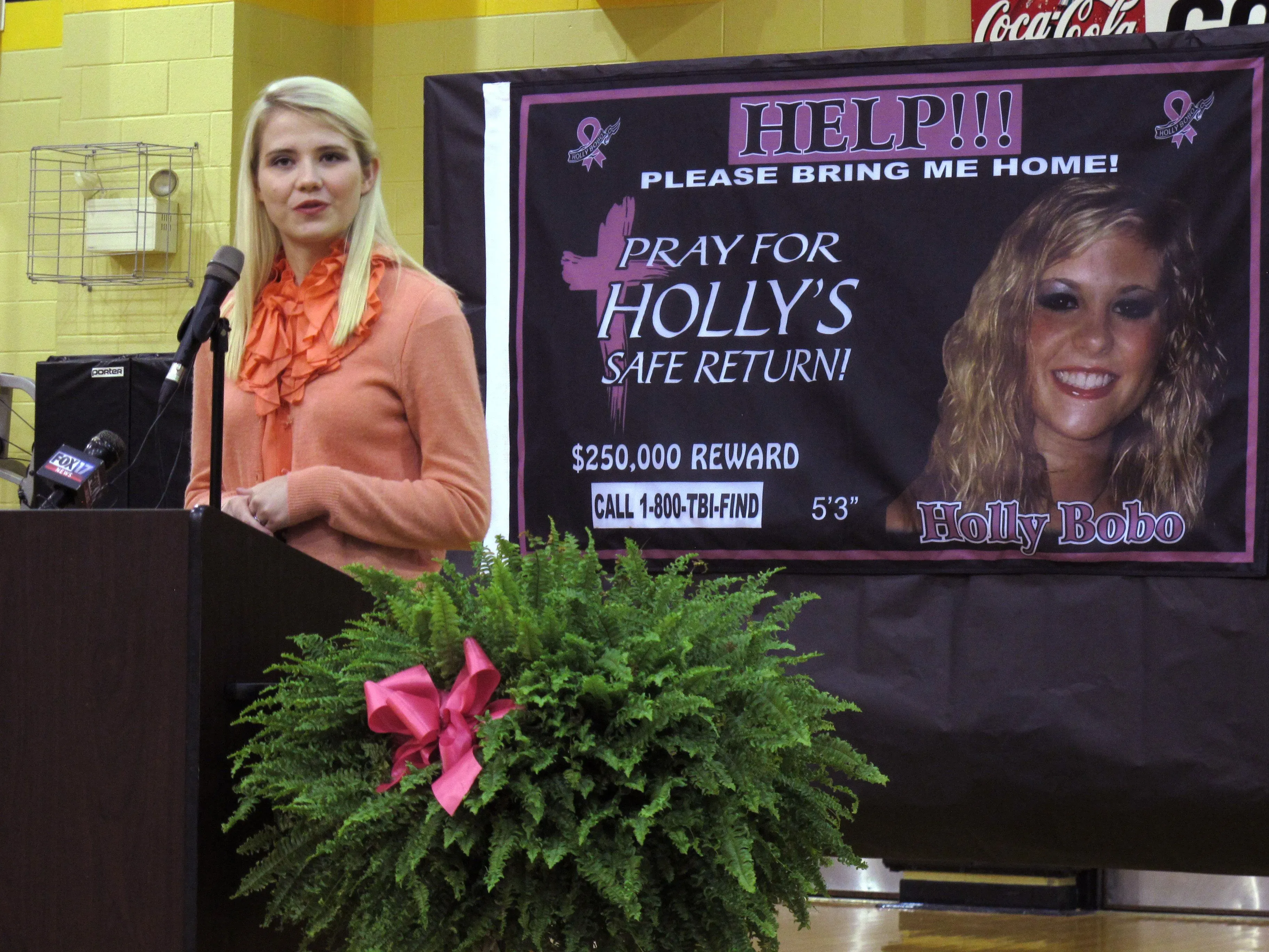 إليزابيث سمارت تتحدث في مؤتمر صحفي، أمام لافتة تطلب المساعدة في العثور على هولي بوبو، مع تفاصيل المكافأة.