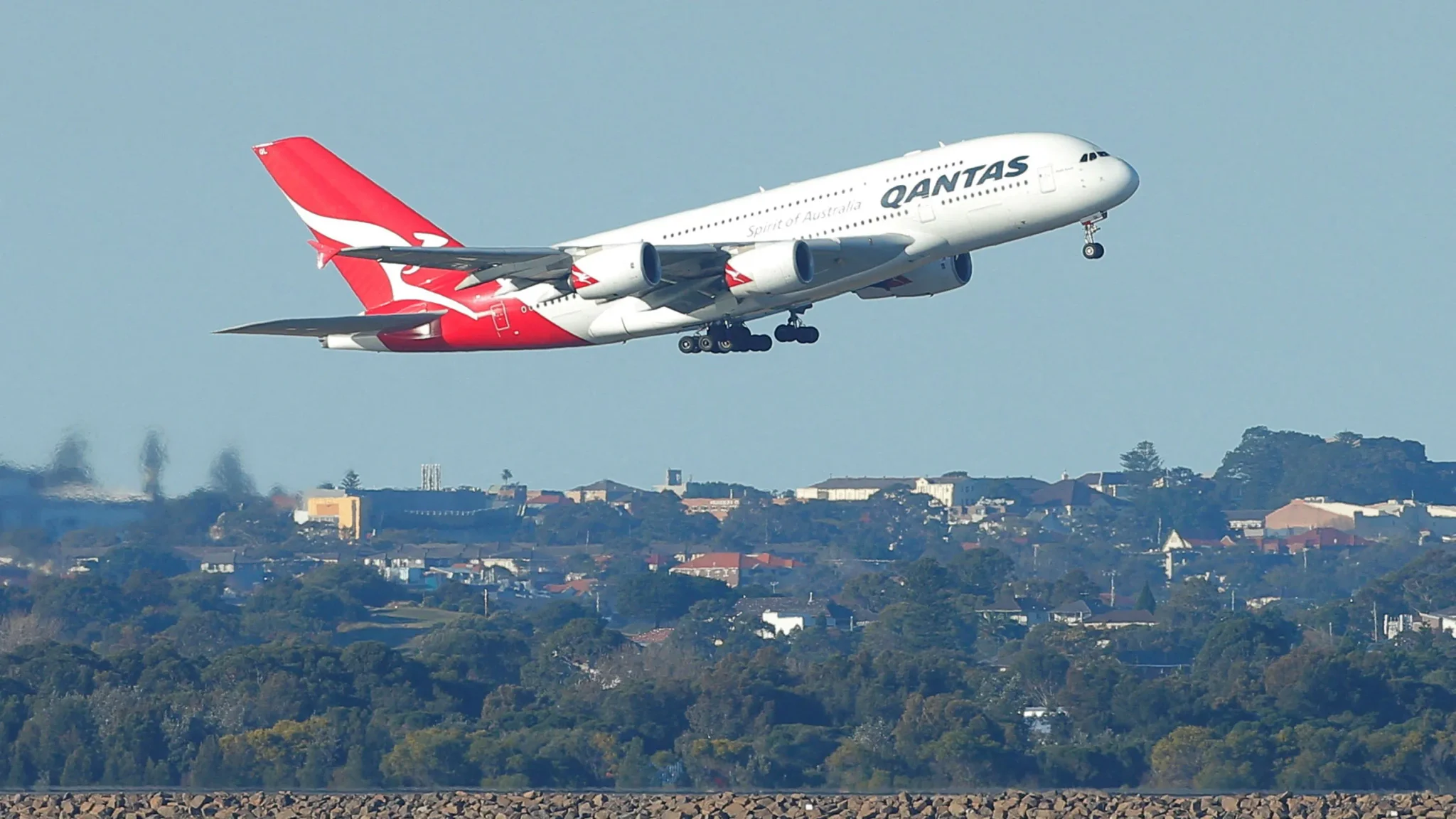 طائرة إيرباص A380 التابعة لشركة كانتاس تقلع فوق مناظر طبيعية حضرية، معبرة عن قرار كانتاس سحب أسطولها من هذا الطراز العملاق قبل الموعد المحدد.