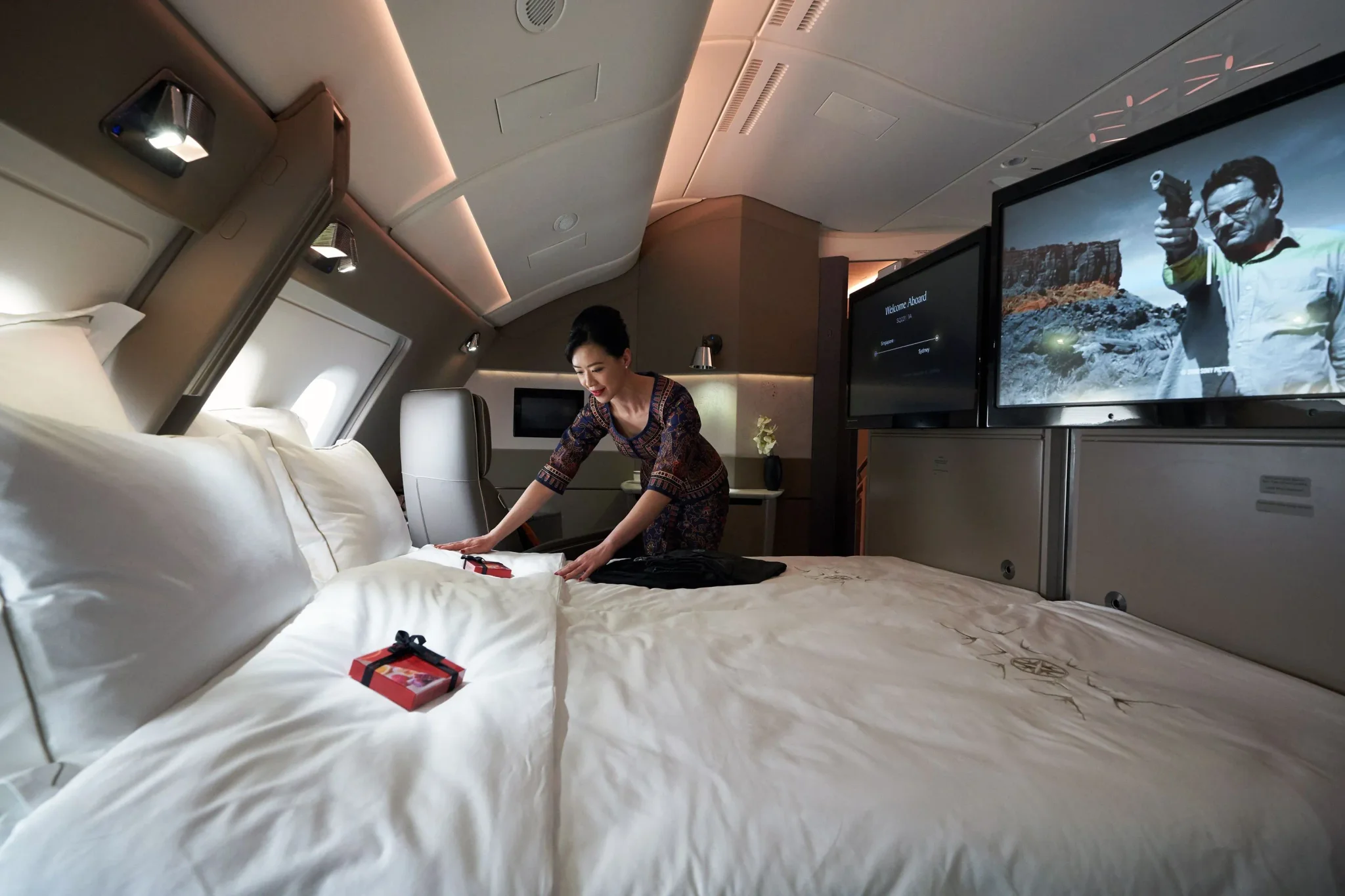 مضيفة تعد السرير الفاخر في جناح خاص داخل طائرة Airbus A380 التابعة لشركة طيران، مع شاشات عرض كبيرة لمشاهدة الأفلام، مما يعكس رفاهية السفر الجوي.