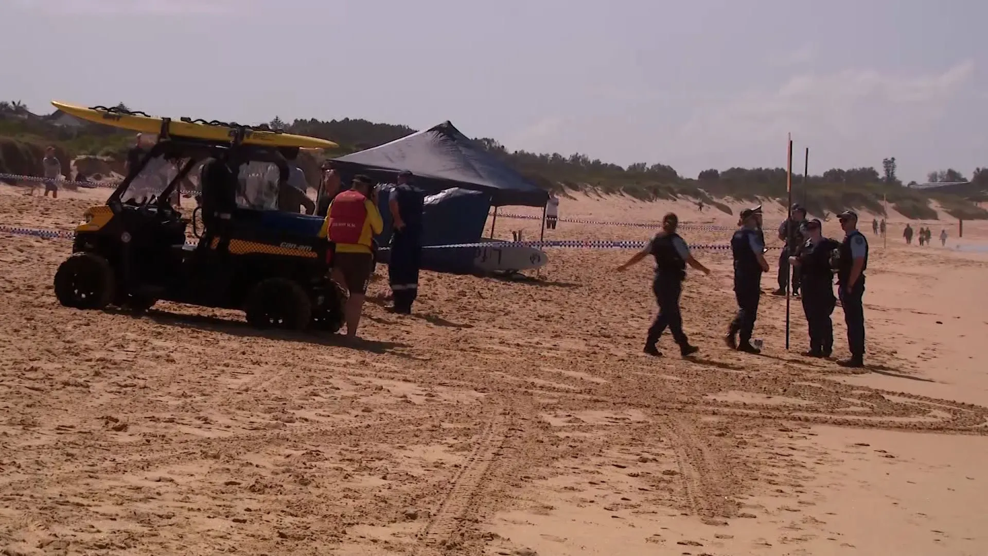 تواجد خدمات الطوارئ والشرطة على شاطئ لونغ ريف بعد هجوم سمكة قرش، مع وجود مركبة إنقاذ وخيمة.