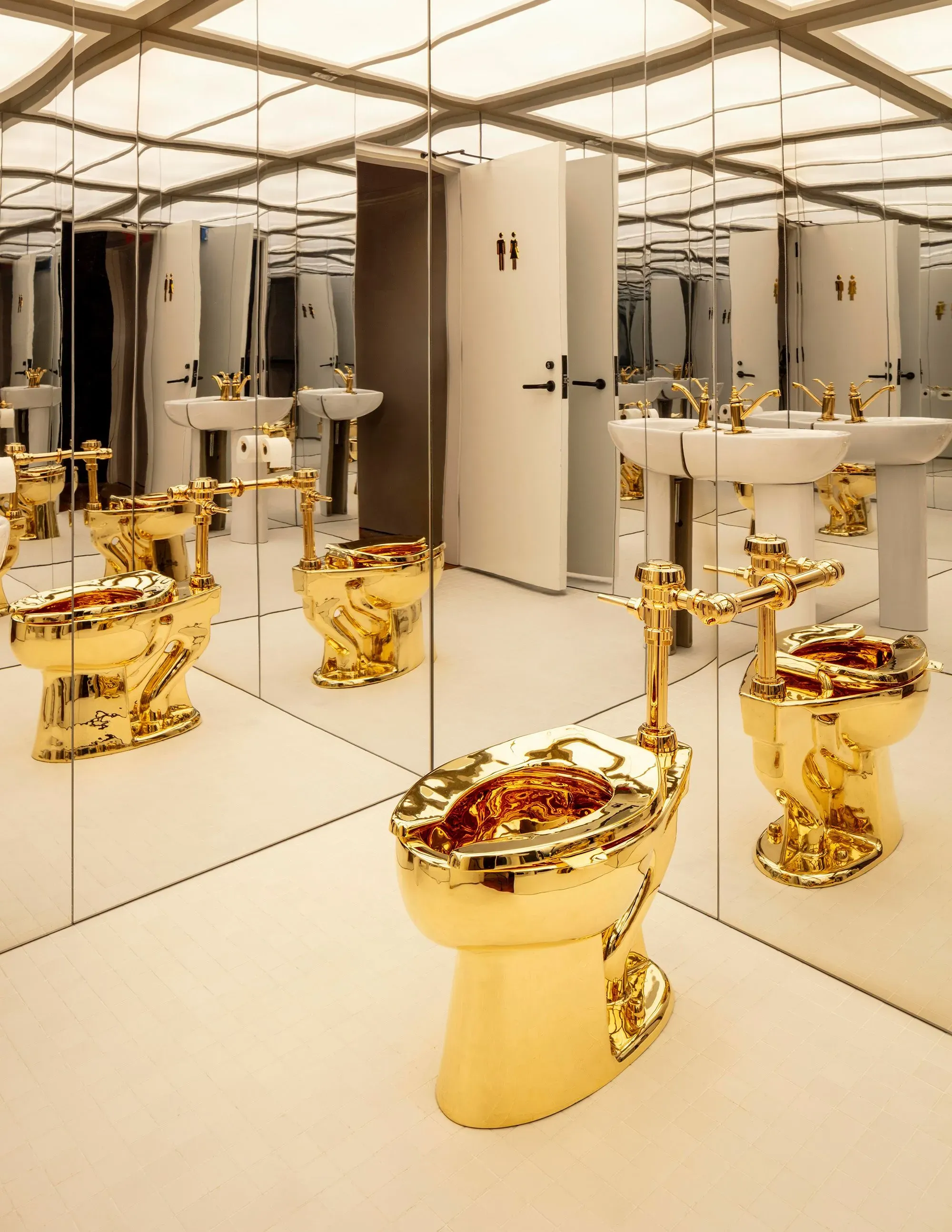 مرحاض ذهبي لامع للفنان ماوريتسيو كاتيلان، محاط بمرايا، يعكس مفهوم القيمة الفنية مقابل القيمة المادية.