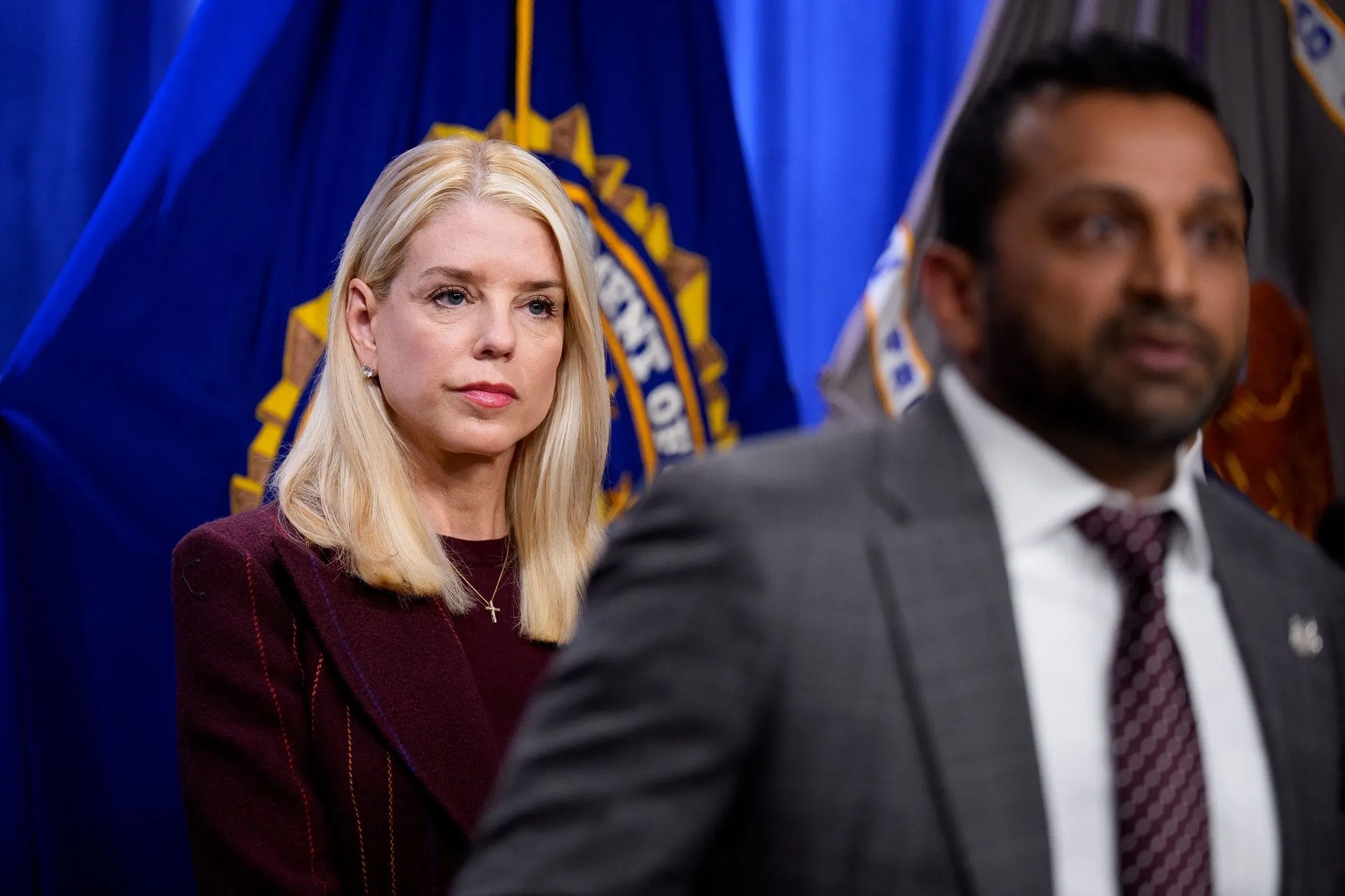 امرأة تنظر بجدية خلال مؤتمر صحفي، مع وجود علم مكتب التحقيقات الفيدرالي خلفها، مما يعكس أهمية القضية المتعلقة بإبشتاين.