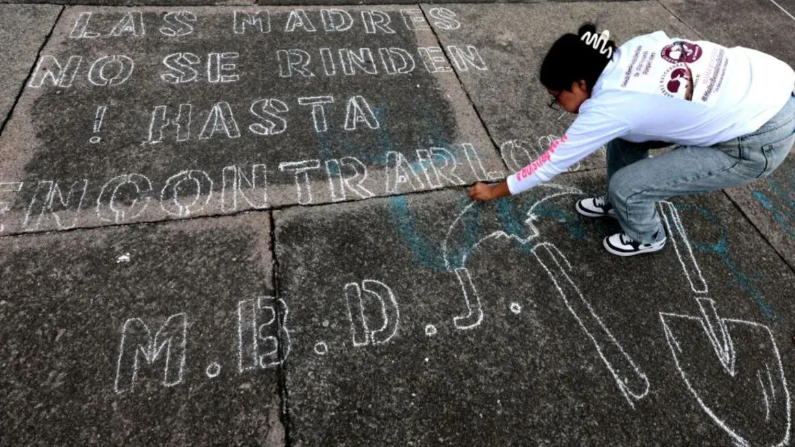 امرأة تكتب على الرصيف باستخدام الطباشير، تعبر عن تصميمها في البحث عن المفقودين، مع عبارة "الأمهات لا يستسلمن! حتى نجدهم".