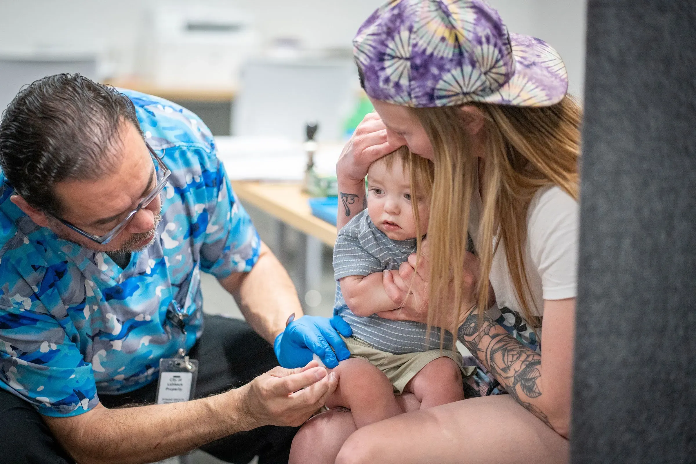 طفل صغير يتلقى لقاحًا من طبيب، بينما تحتضنه والدته. تعكس الصورة أهمية التطعيم في حماية الأطفال من الأمراض.