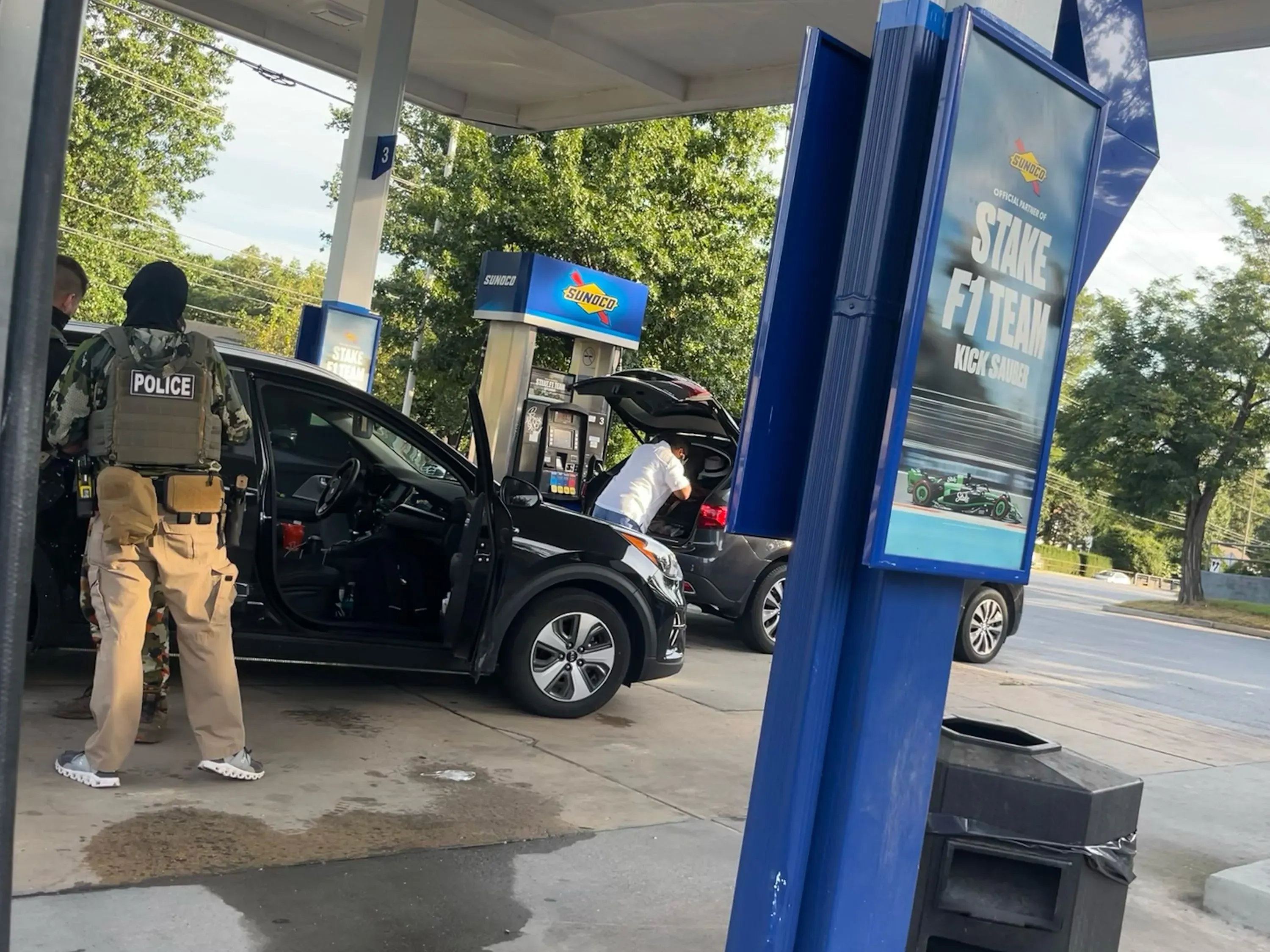 عملية اعتقال من قبل وكالة إنفاذ قوانين الهجرة والجمارك في محطة وقود، مع وجود رجال ملثمين وشرطة.