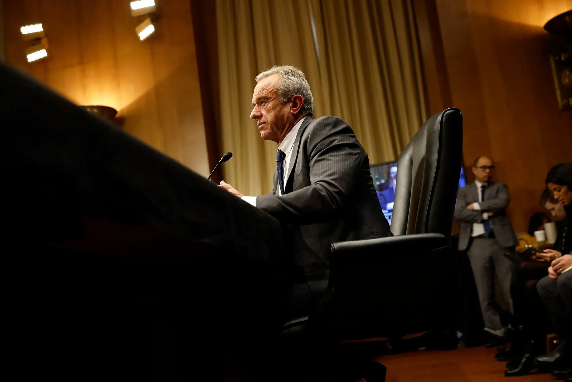 روبرت ف. كينيدي جونيور يجلس في جلسة استماع، مع التركيز على تعبيره الجاد وسط توتر سياسي حول إدارة الصحة العامة.