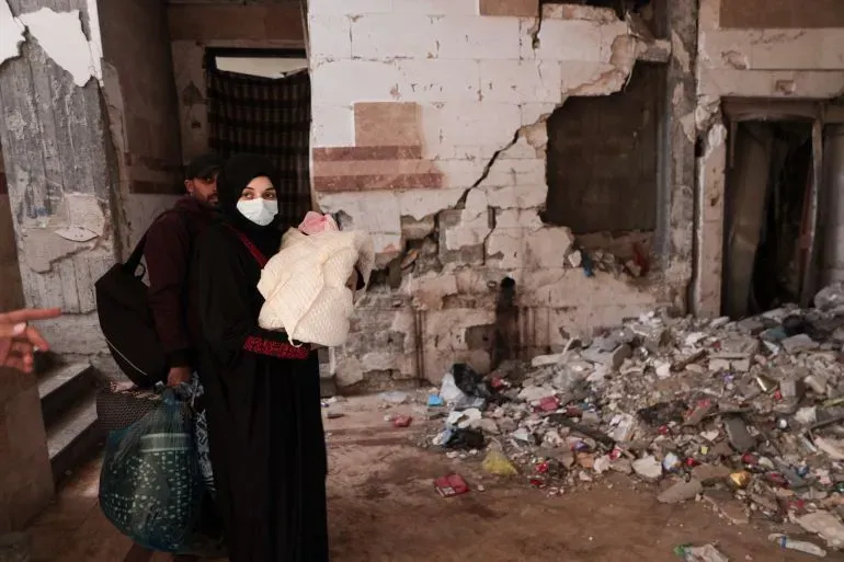 امرأة ترتدي كمامة وتحمل مولودها الجديد في شقة مهدّمة، تعكس معاناتها تحت وطأة الحرب وفقر الغذاء في غزة.