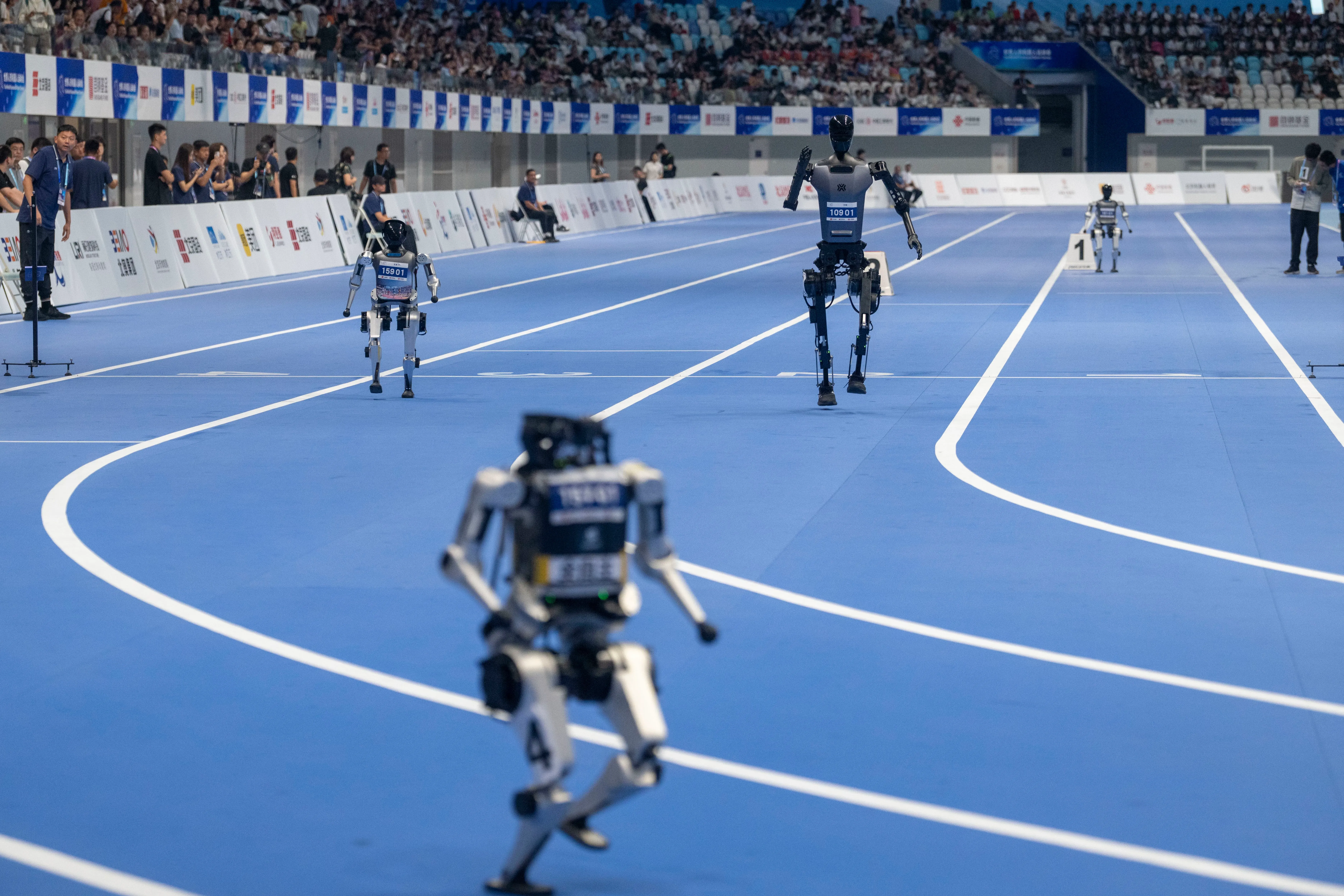 تتنافس عدة روبوتات في سباق على مضمار أزرق، مع جمهور في الخلفية، خلال دورة الألعاب العالمية للروبوتات في بكين.