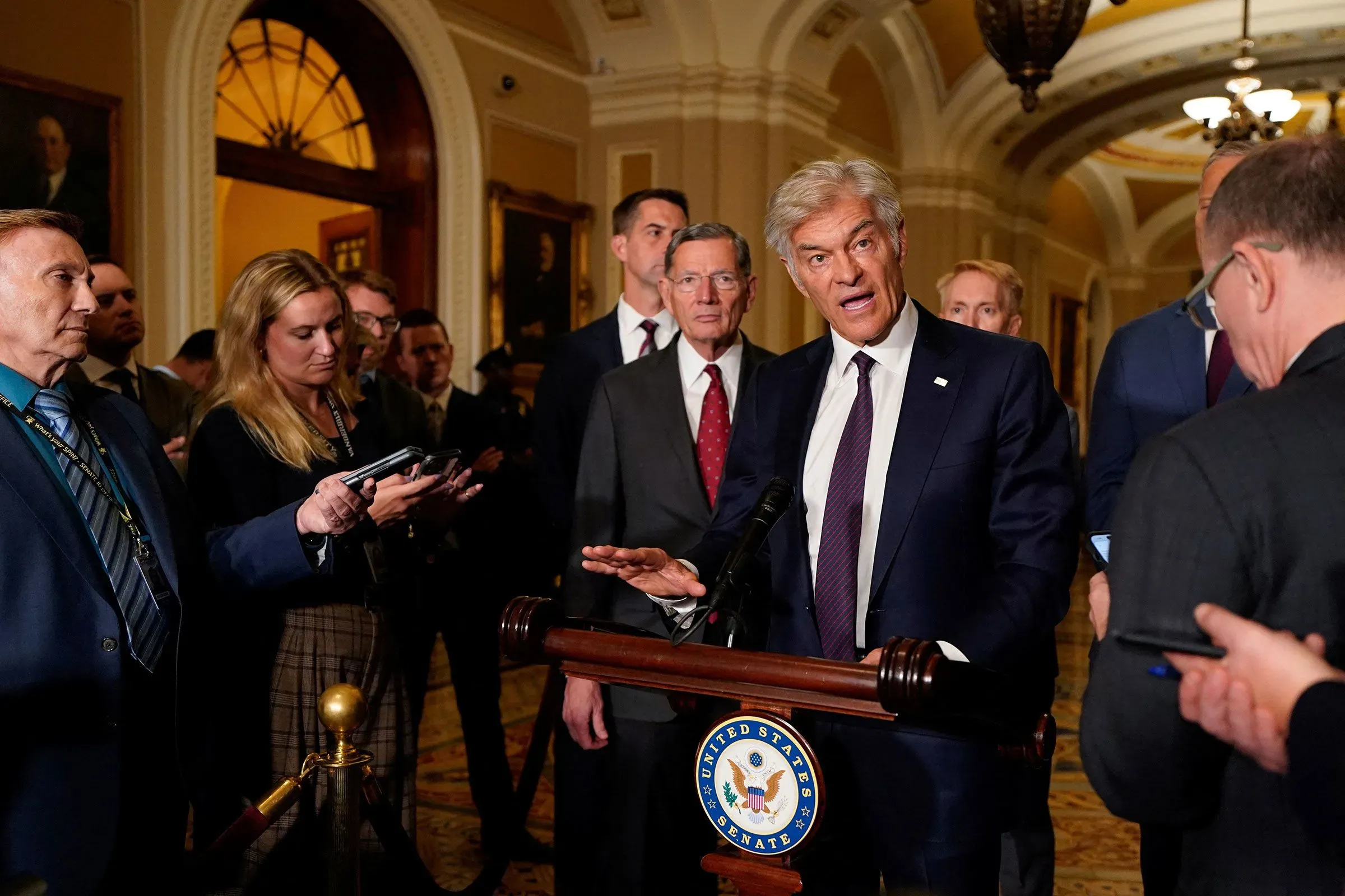 مؤتمر صحفي في مبنى الكابيتول، حيث يتحدث مسؤول حكومي أمام مجموعة من الصحفيين، مع التركيز على قضايا الرعاية الصحية الريفية.