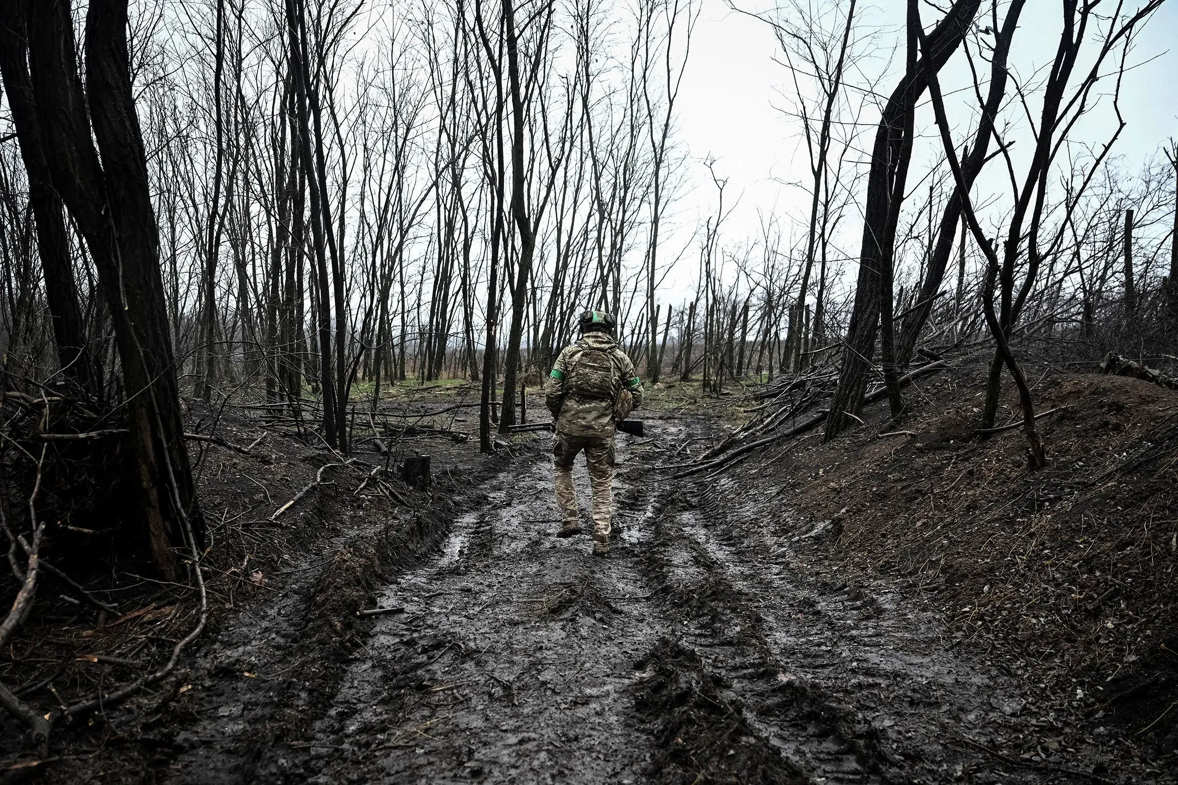جندي يسير في طريق موحل بين أشجار متفحمة، يعكس آثار الصراع في بوكروفسك شرقي أوكرانيا.