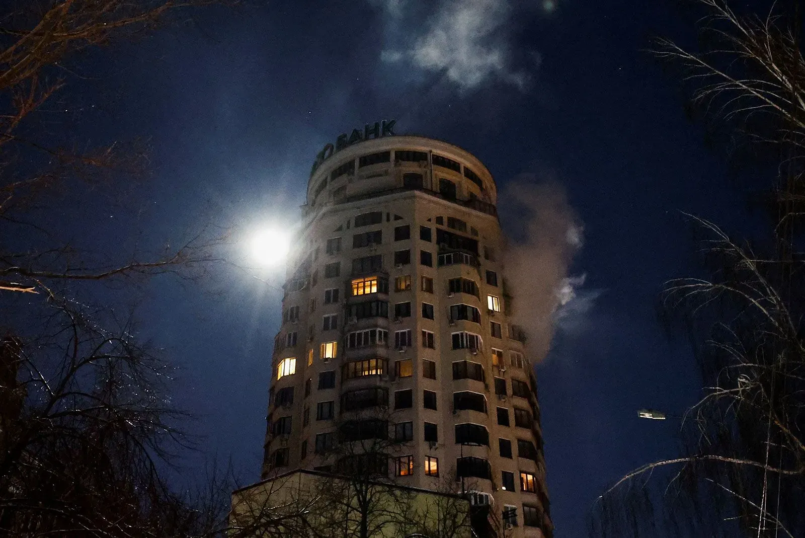 عمارة سكنية في كييف تتعرض للهجوم، مع تصاعد الدخان من الأعلى، وتظهر الأضواء في النوافذ، في ظل ظروف شتوية قاسية.
