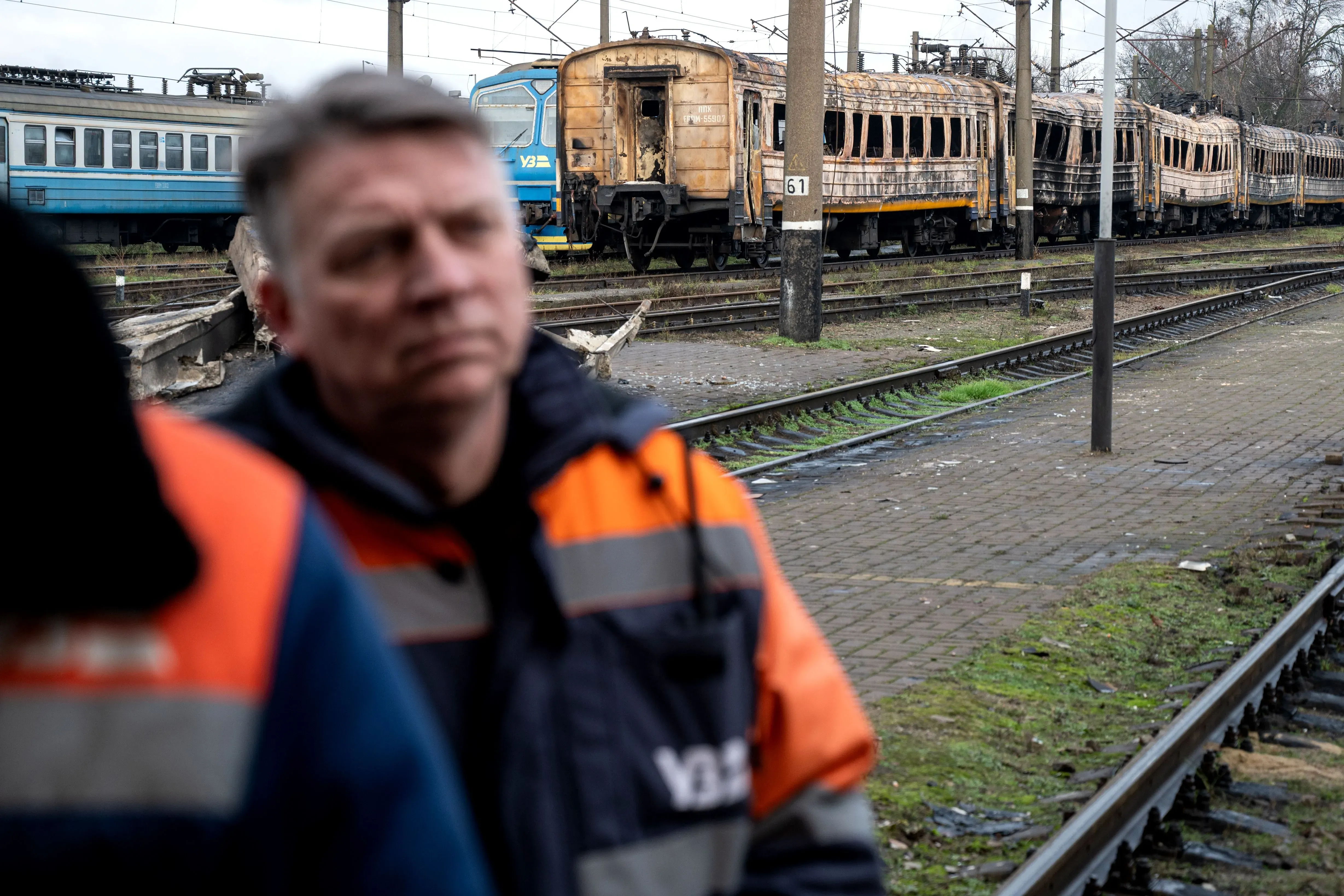 عمال السكك الحديدية في أوكرانيا يقفون أمام عربات قطار متضررة، مما يعكس تأثير الحرب على البنية التحتية للنقل.