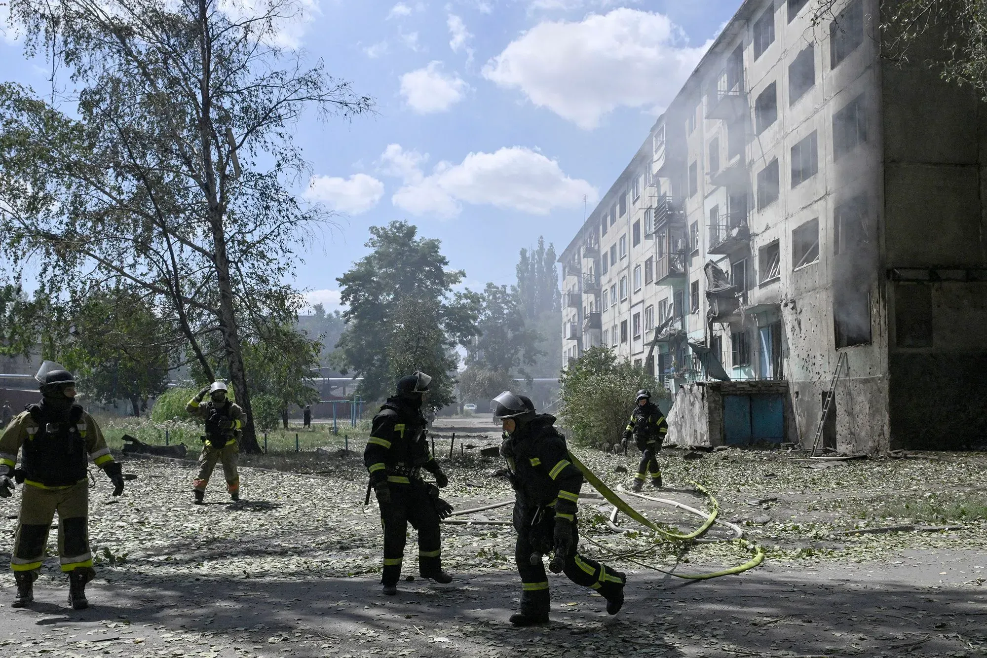 رجال إطفاء يرتدون ملابس واقية يعملون على إخماد حريق في منطقة سكنية متضررة في دونيتسك، مع وجود دمار واضح في المباني المحيطة.