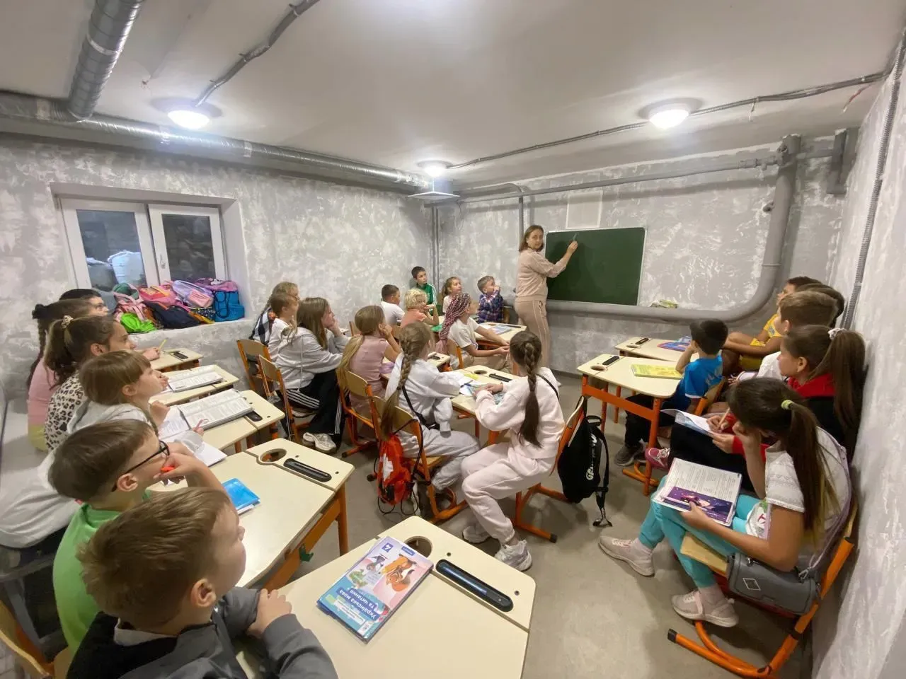 فصل دراسي تحت الأرض في مدرسة كييف، حيث يتلقى الأطفال التعليم وسط التهديدات الجوية، مع معلمة تكتب على السبورة.