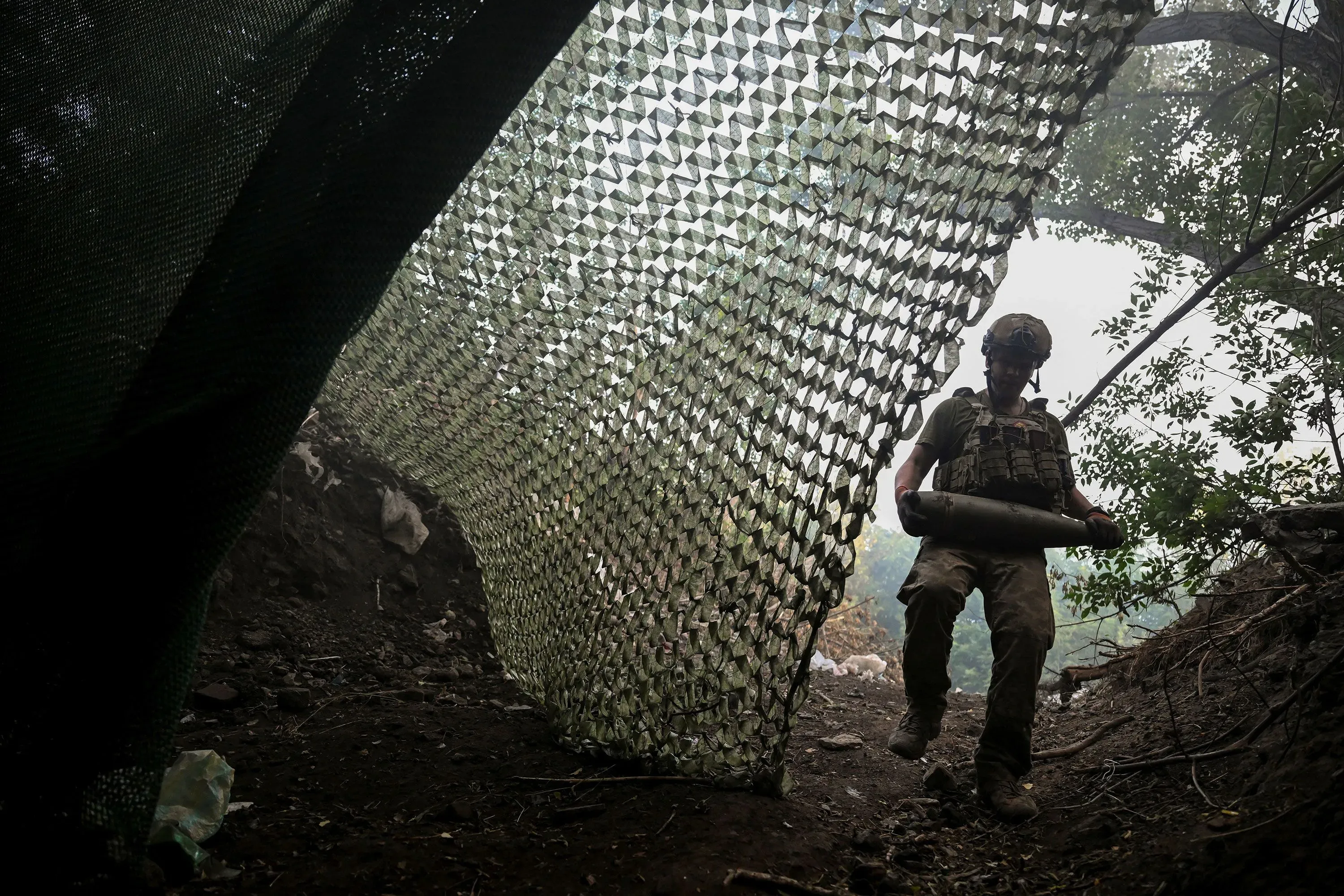 جندي أوكراني يحمل قذيفة بينما يتواجد في موقع محصن تحت شبكة تمويه، وسط أجواء مشحونة بالقتال في منطقة بوكروفسك.