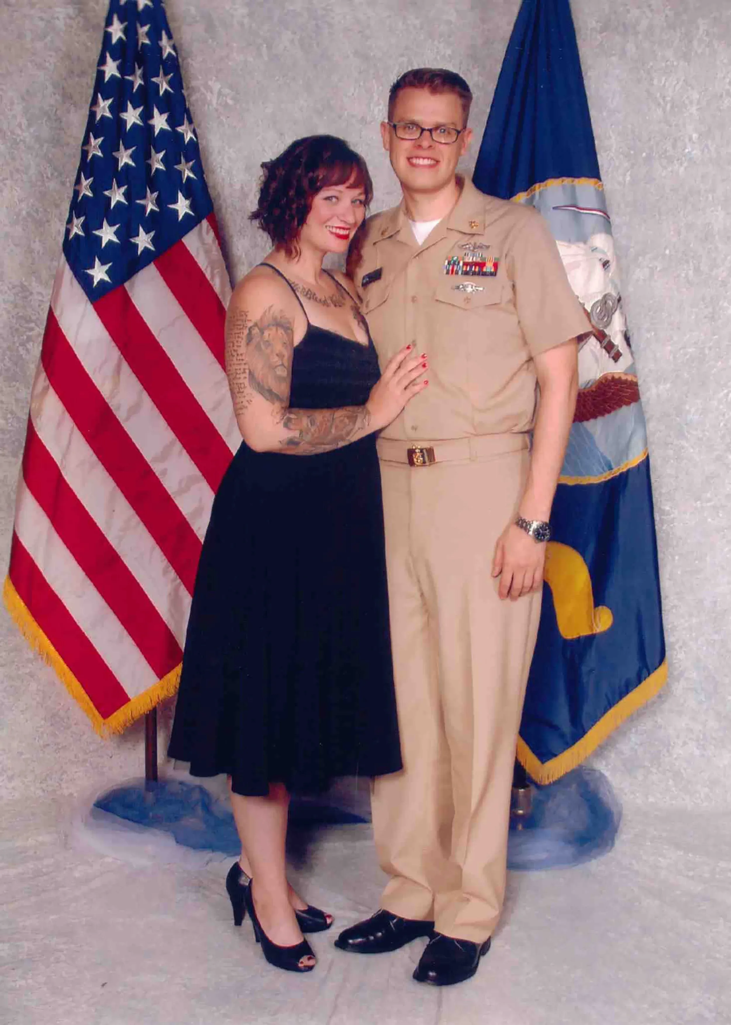 صورة لزوجين مبتسمين، حيث ترتدي الزوجة فستانًا أسود وتظهر بجانبه علم الولايات المتحدة، تعكس لحظات من الحب والدعم في حياتهم.