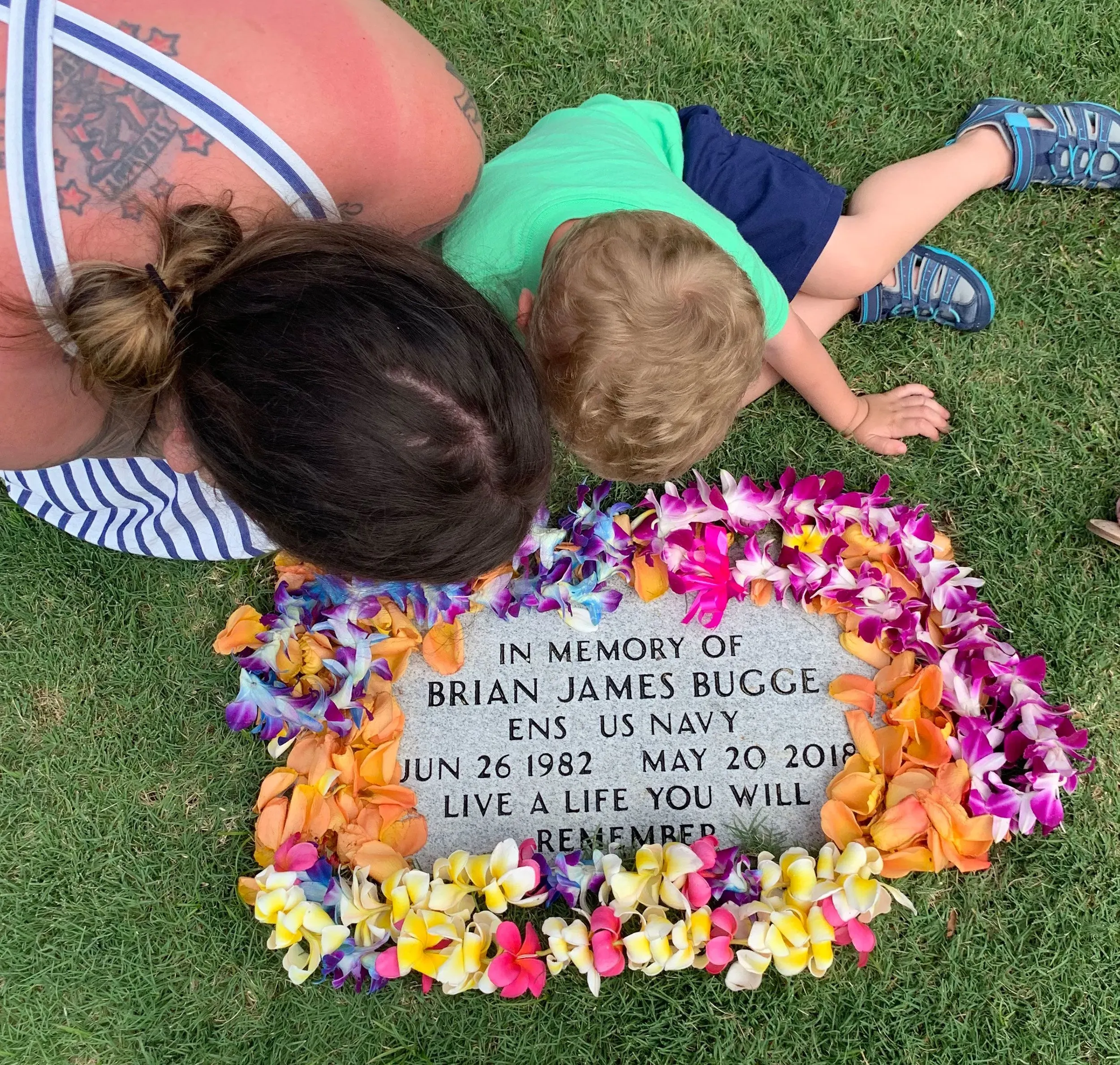 تظهر الصورة امرأة وطفلًا صغيرًا يضعان الزهور حول قبر يحمل اسم "براين جيمس بوج"، الذي توفي أثناء الغوص.