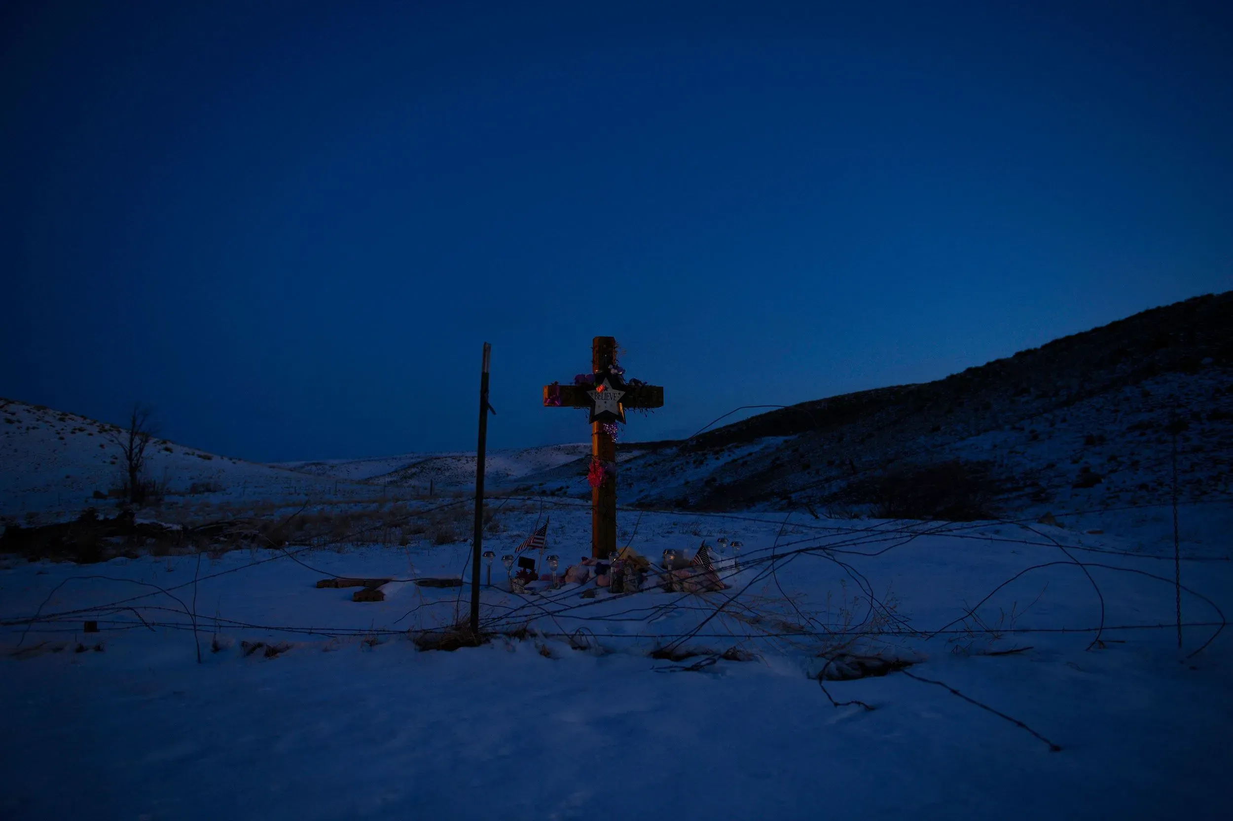صليب خشبي مزين بالزهور والأعلام في منطقة ثلجية مظلمة، يرمز إلى ذكرى جيسيكا ريدجواي، التي اختفت في 2012.
