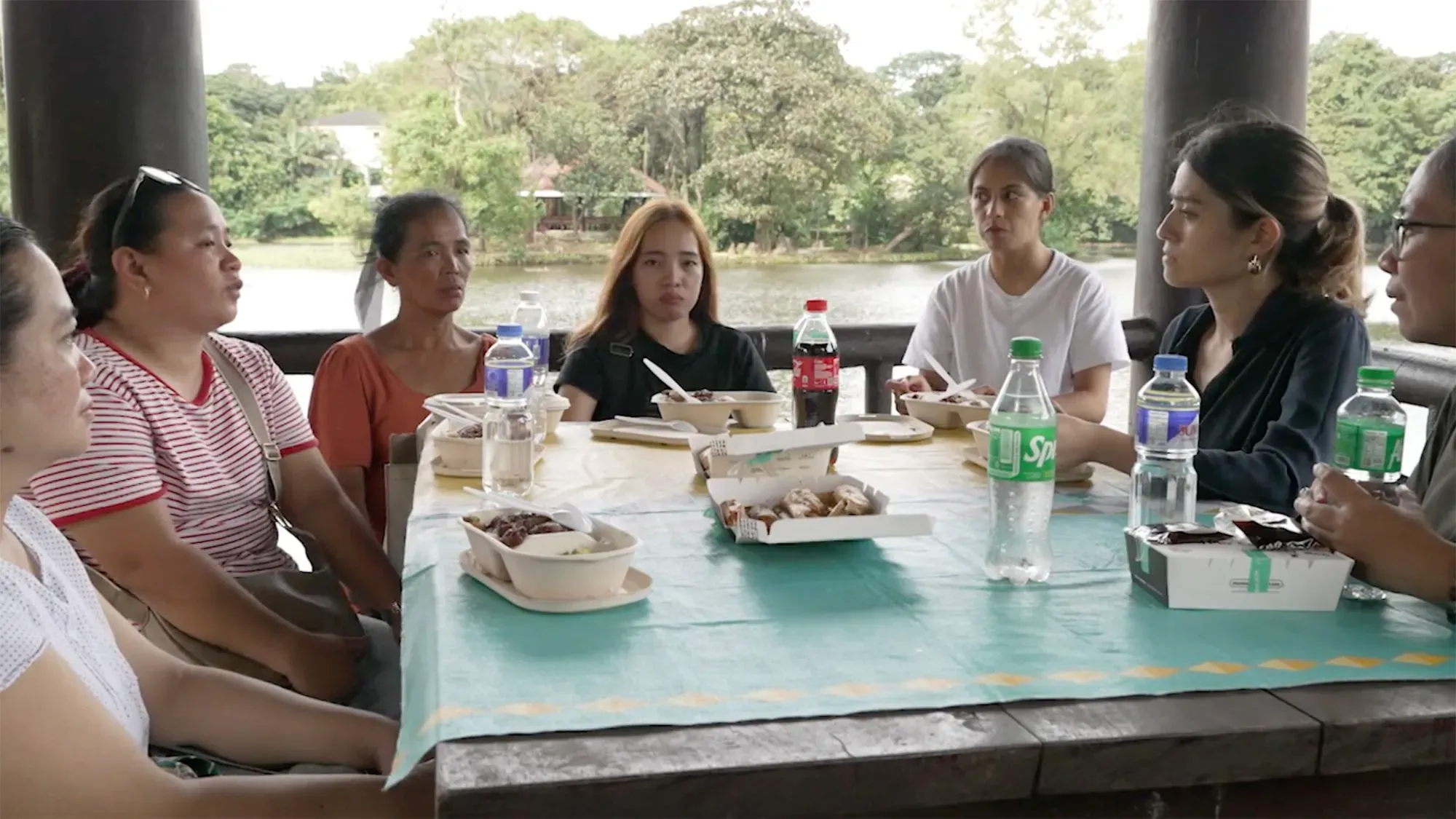 مجموعة من النساء يجلسن حول طاولة في مكان مفتوح، يتناولن الطعام ويشاركن تجاربهن حول الاتجار بالبشر والاحتيال.