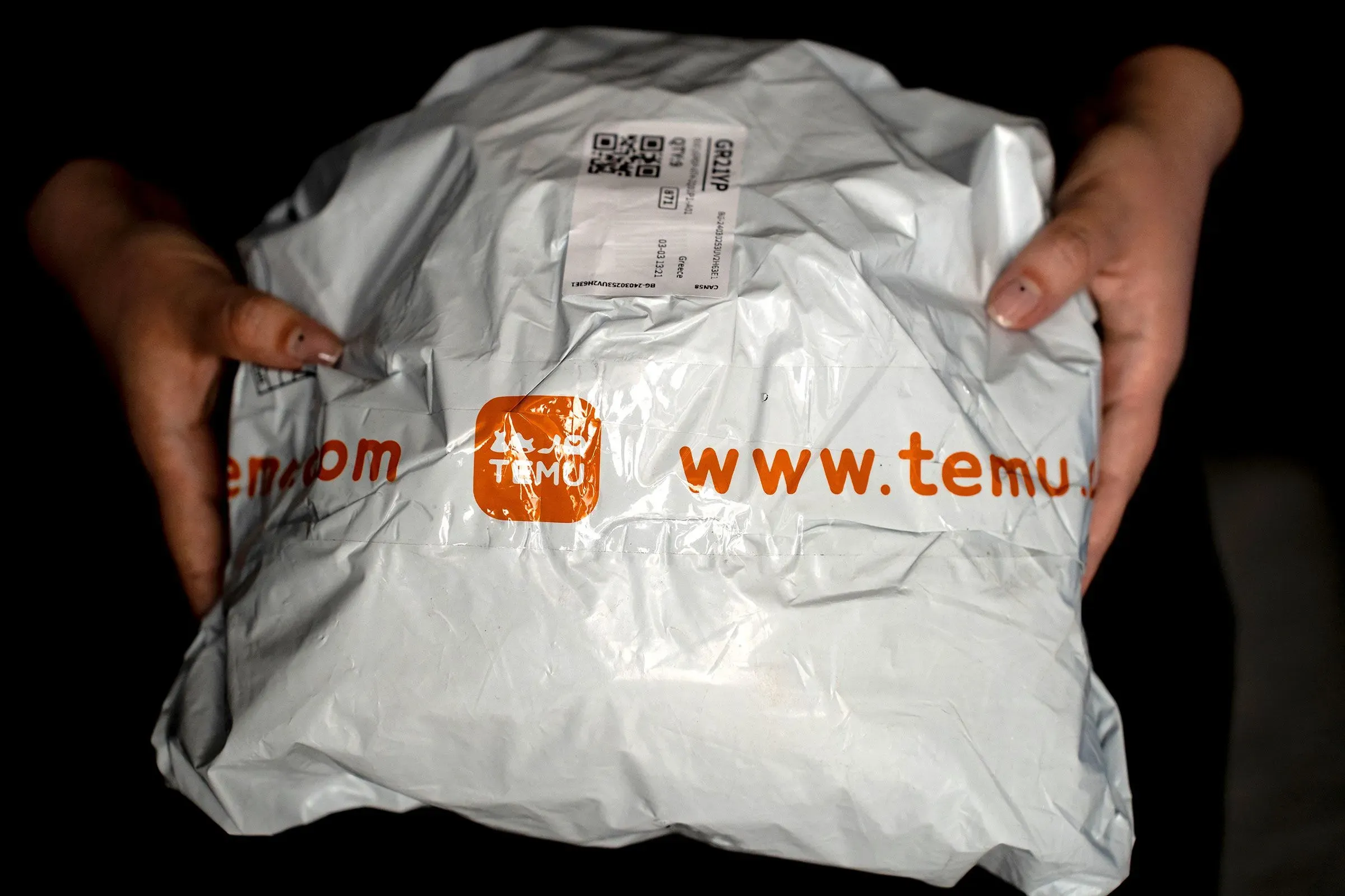 حزمة شحن تحمل شعار "Temu" في يد شخص، تعكس تأثير التغييرات في الرسوم الجمركية على التجارة الإلكترونية.