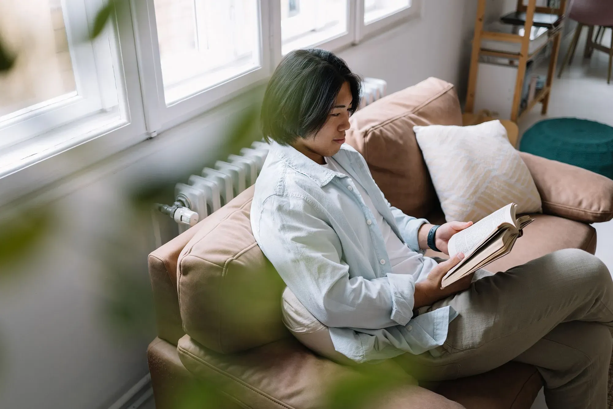 شخص يجلس على أريكة ويقرأ كتابًا في غرفة مضاءة جيدًا، مما يعكس أهمية القراءة كجزء من برنامج 75 Hard لتعزيز العادات الصحية.