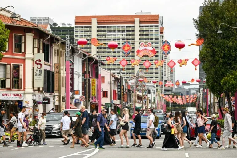 مشهد نابض بالحياة في سنغافورة، حيث يعبر مجموعة من الأشخاص الشارع وسط أجواء احتفالية مع زينة تقليدية وأبنية حديثة.