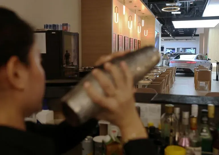 داخل صالة عرض BYD في سنغافورة، تظهر سيارة كهربائية أنيقة في الخلفية بينما يهتم موظف بمشروبات الزبائن في أجواء مستقبلية.