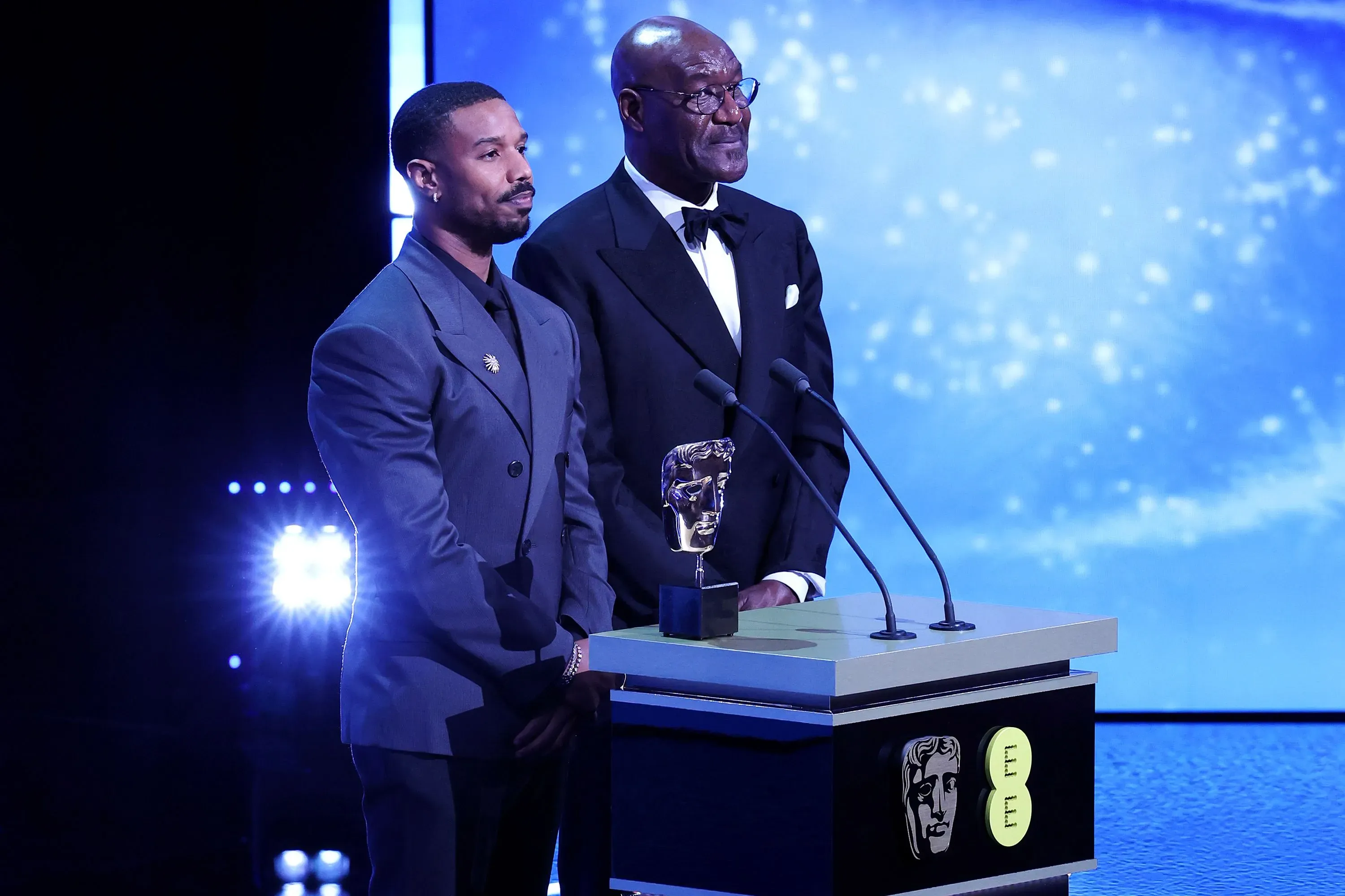 مايكل بي جوردان وديلروي ليندو على المسرح في حفل توزيع جوائز البافتا، حيث يقدمان جائزة وسط أضواء ساطعة.