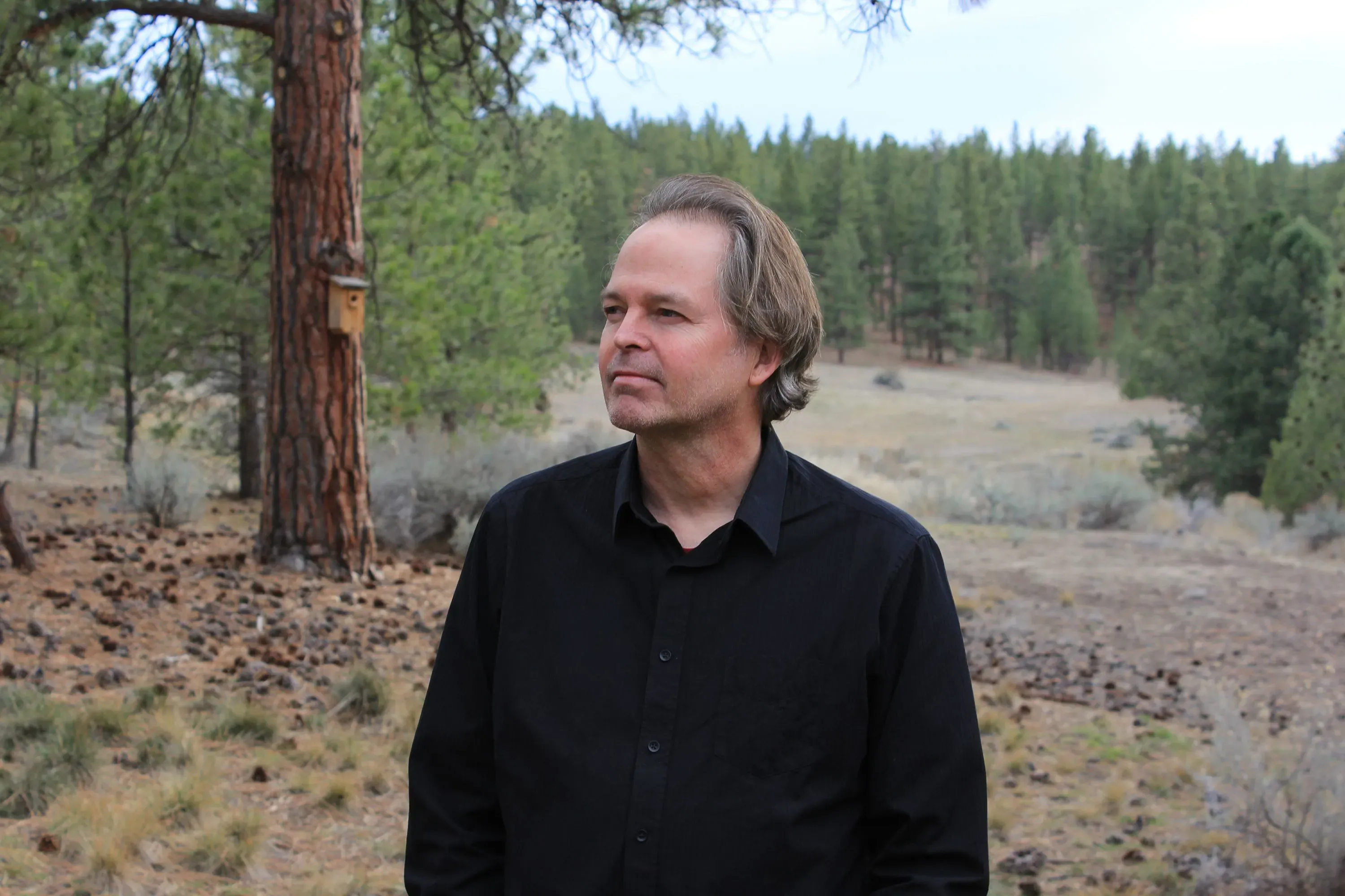 رجل يرتدي قميصًا أسود يقف في منطقة طبيعية محاطة بأشجار، يعكس التأثيرات السلبية على العلوم بسبب تغييرات في إدارة ترامب.