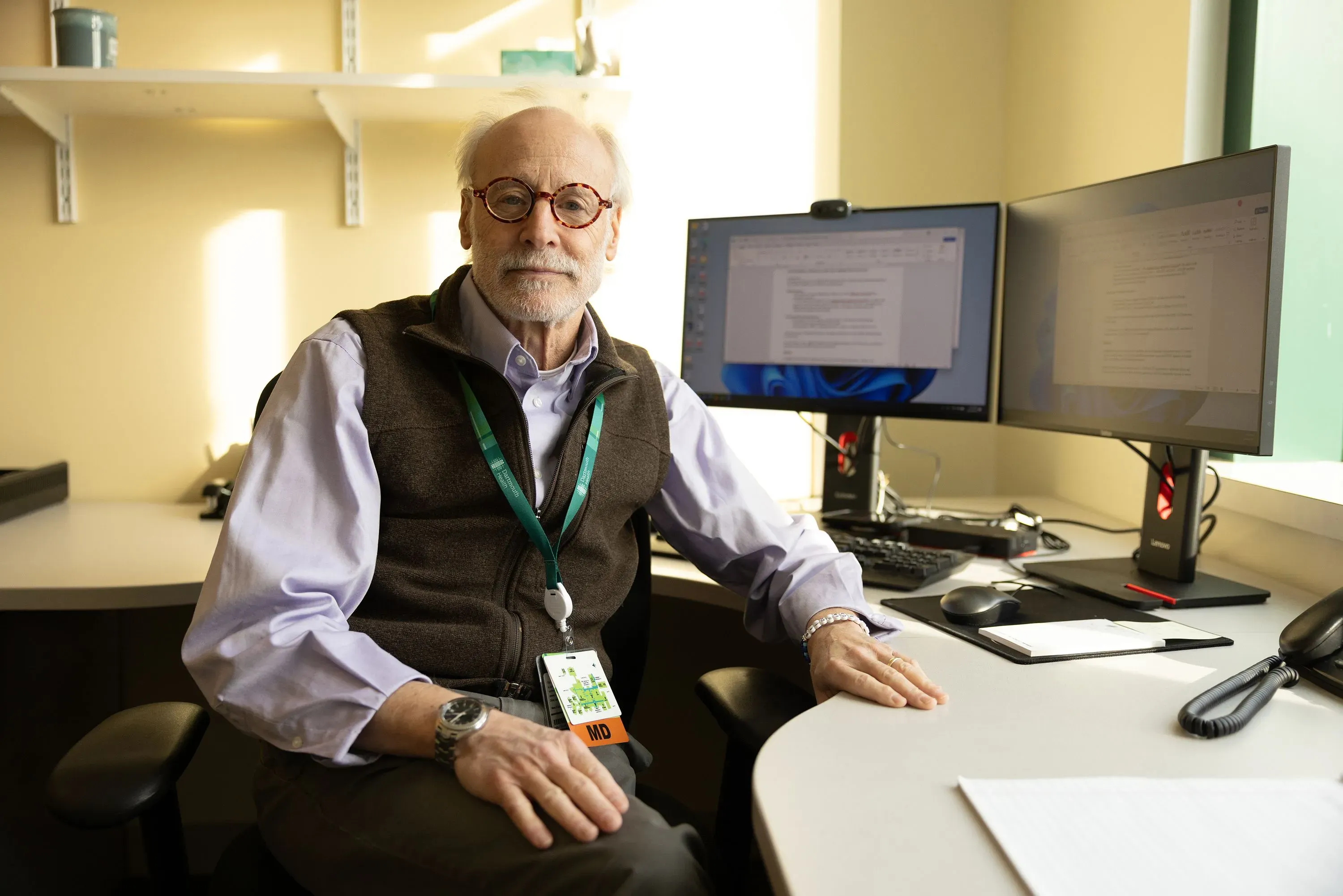 عالم يجلس أمام مكتبه في مختبر، محاط بشاشات كمبيوتر، يعكس تأثير نقص التمويل على أبحاث الصحة العامة.