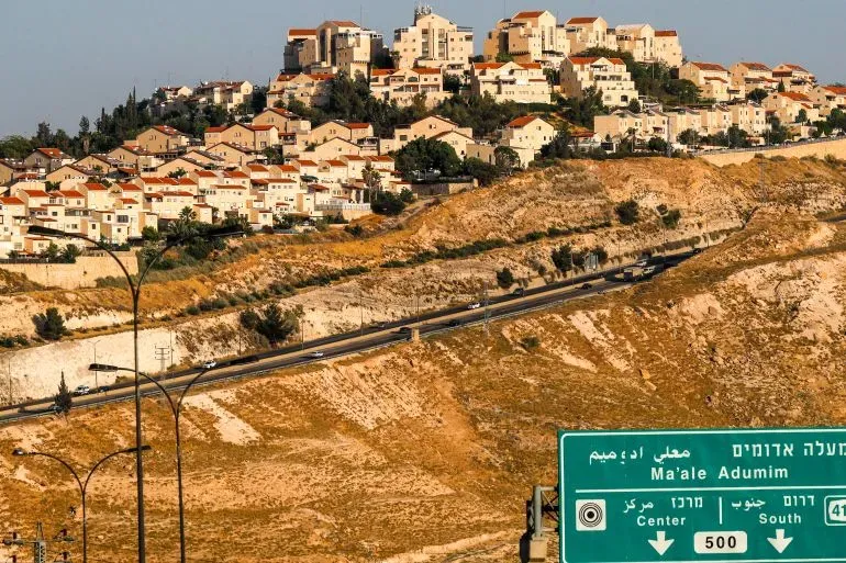 مشهد لمستوطنة معاليه أدوميم في الضفة الغربية، يظهر المنازل والمباني الجديدة، مع لافتة توجيه تشير إلى الاتجاهات.