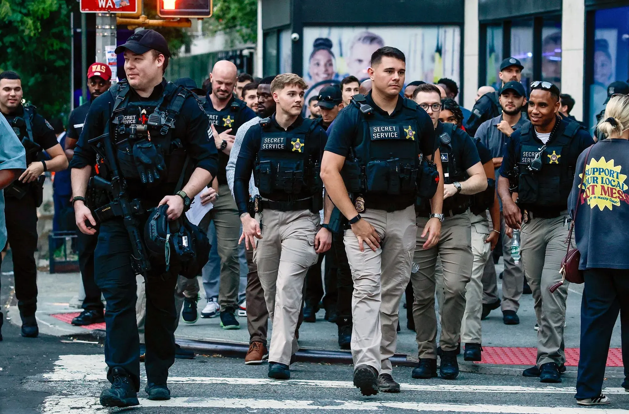 مجموعة من عناصر الخدمة السرية يرتدون زيهم الرسمي ويقومون بتأمين منطقة مزدحمة، وسط مخاوف من تهديدات القناصة في الأحداث العامة.