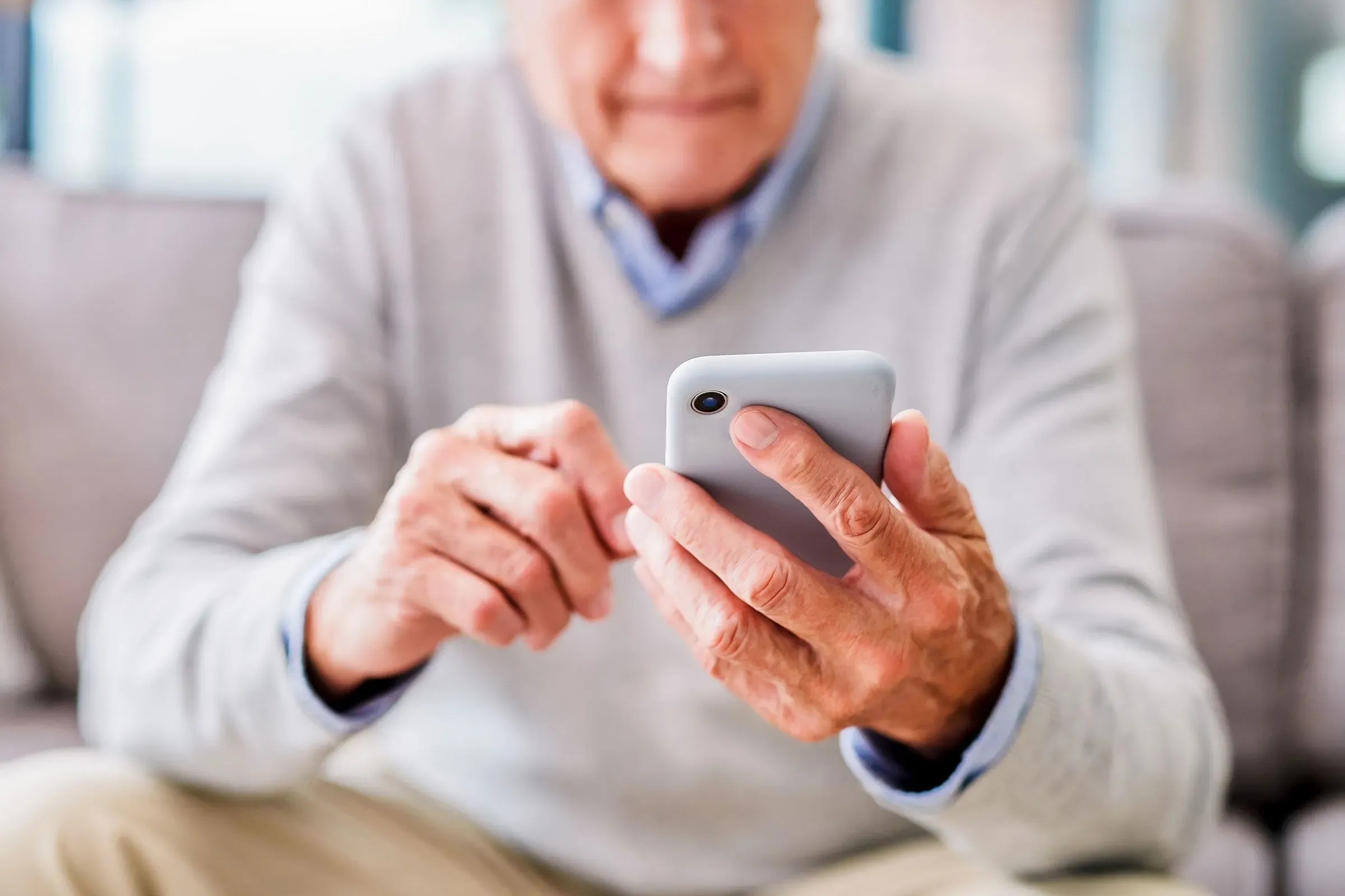 رجل مسن يستخدم هاتفه المحمول في المنزل، مع التركيز على أهمية الوصول إلى خدمات الضمان الاجتماعي وتحسين أوقات الانتظار.