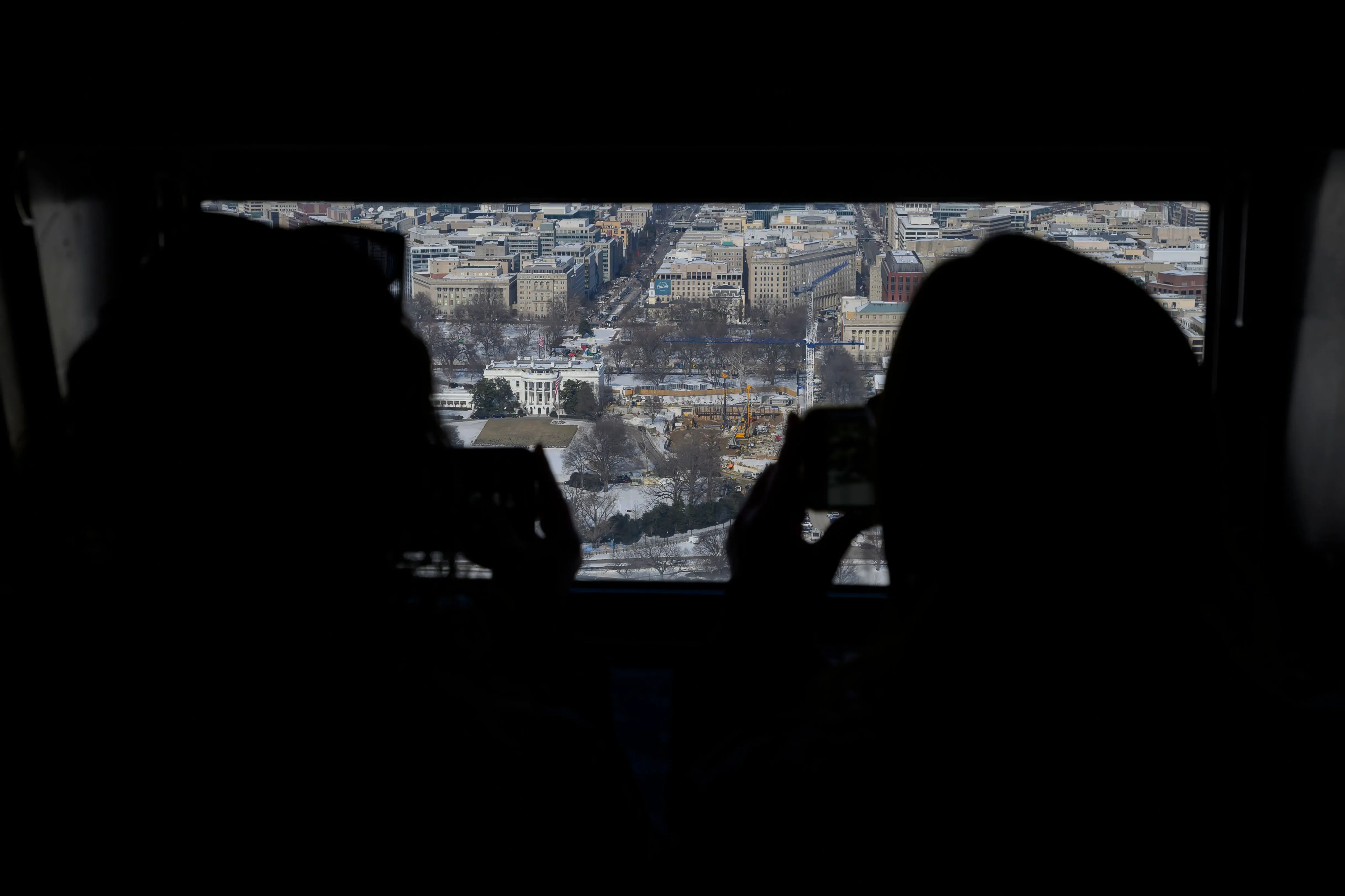 منظر لمدينة واشنطن مع silhouettes لشخصين يلتقطان صورًا، يظهر البيت الأبيض في الخلفية مع أعمال بناء جارية حوله.