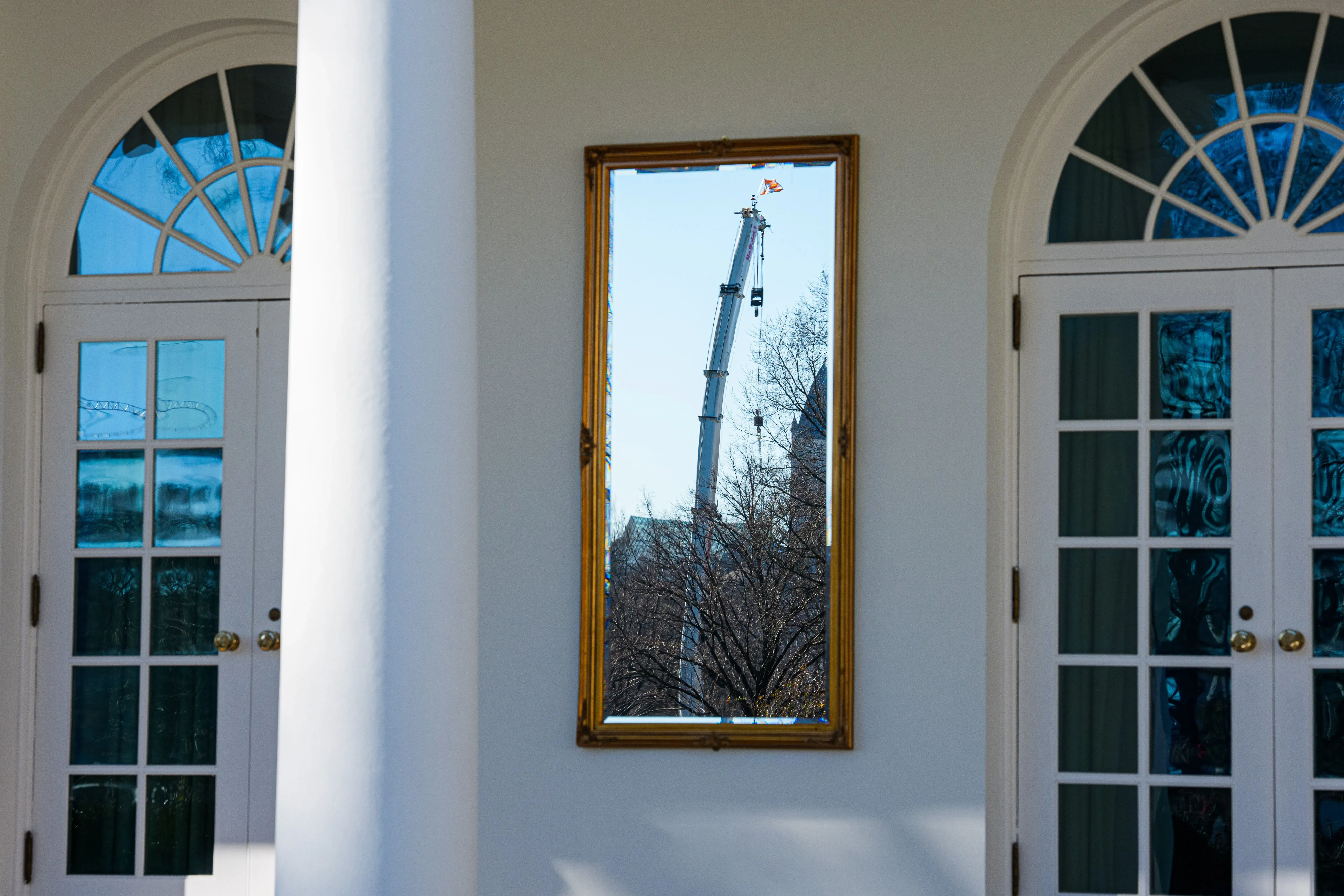 انعكاس رافعة في إطار ذهبي، يظهر جزء من الجناح الشرقي للبيت الأبيض، مع أبواب زجاجية مزدوجة في المقدمة.