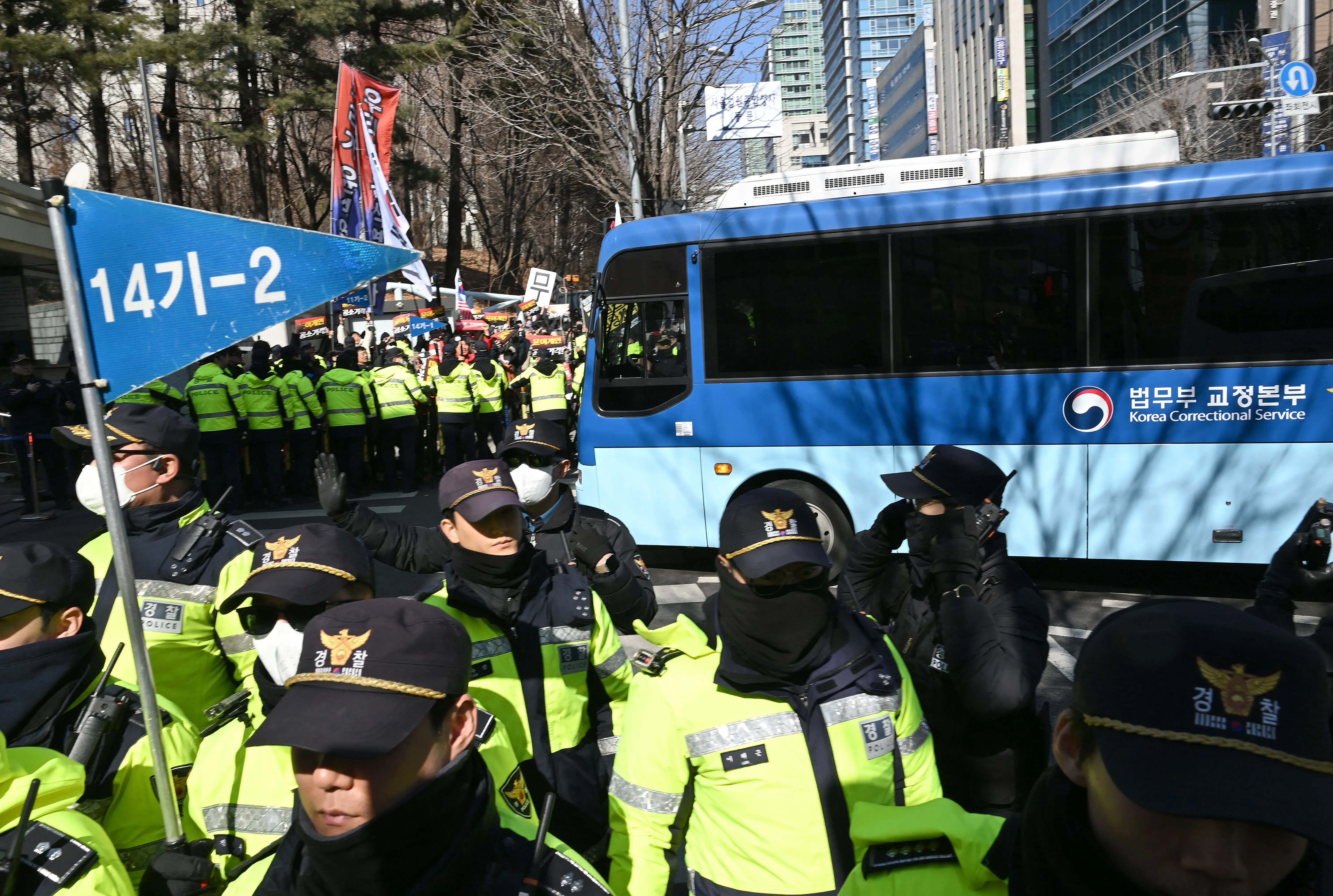 تجمع حشود من الشرطة في سيول، حيث يرتدي الضباط زيًا موحدًا ويحيطون بحافلة تابعة لهيئة السجون الكورية، وسط توتر سياسي.