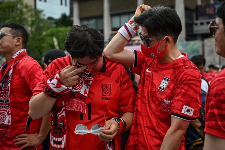 مشجعون كوريون يرتدون قمصان المنتخب الوطني ويعبرون عن الحزن والإحباط بعد خروج كوريا الجنوبية المبكر من كأس العالم 2024.