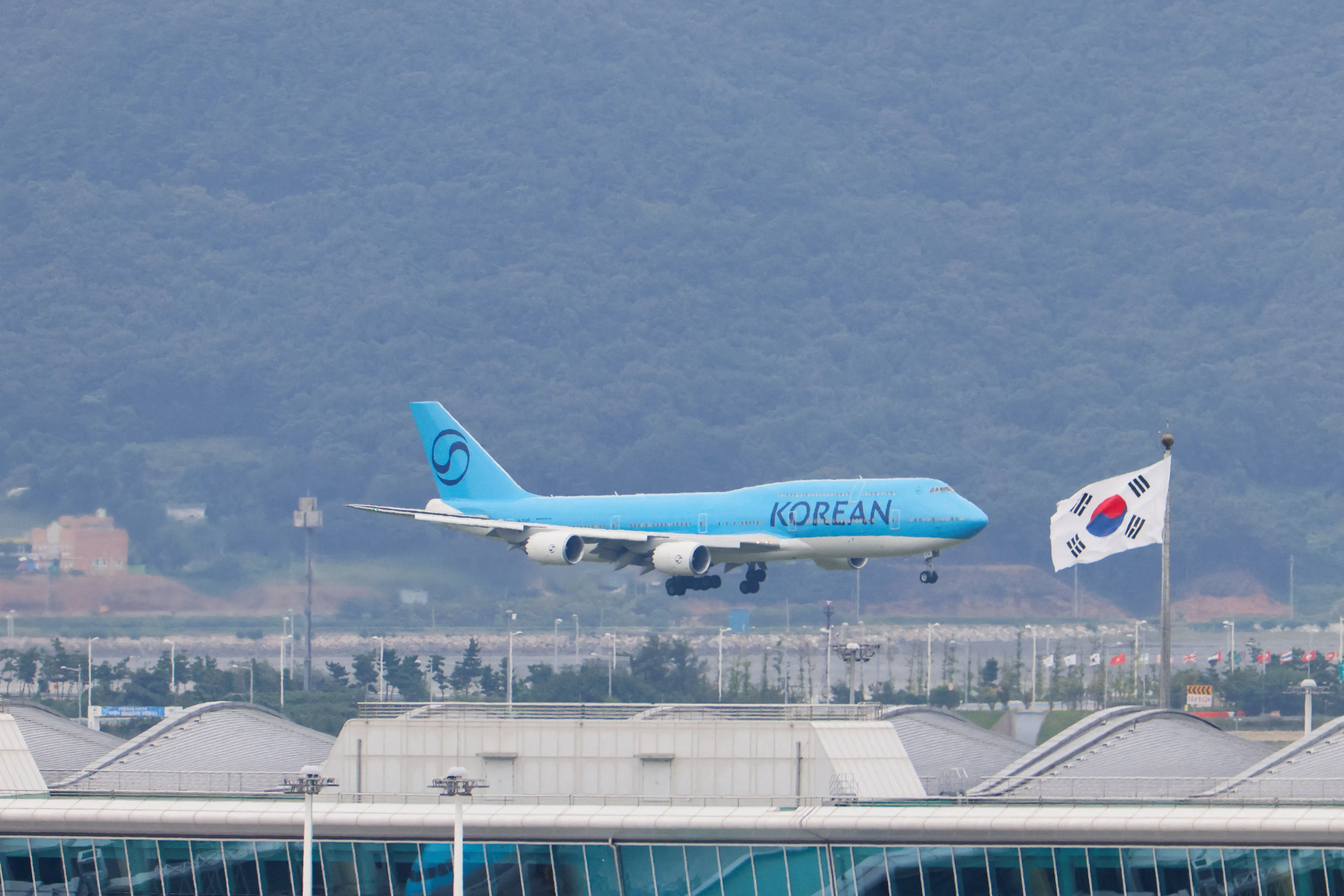 طائرة كورية تقترب من الهبوط في مطار سيول الدولي، مع علم كوريا الجنوبية يرفرف بجانبها، في لحظة عودة العمال المحتجزين.