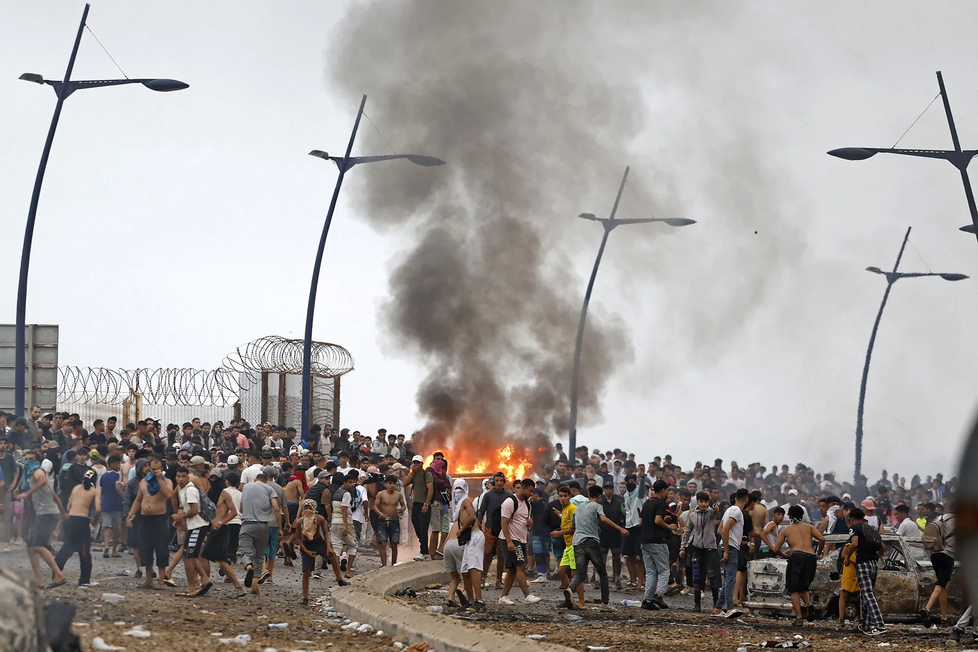 حشود كبيرة من المهاجرين عند الحدود بين المغرب وسبتة الإسبانية وسط دخان ناتج عن حريق خلال موجة اقتحام غير مسبوقة.