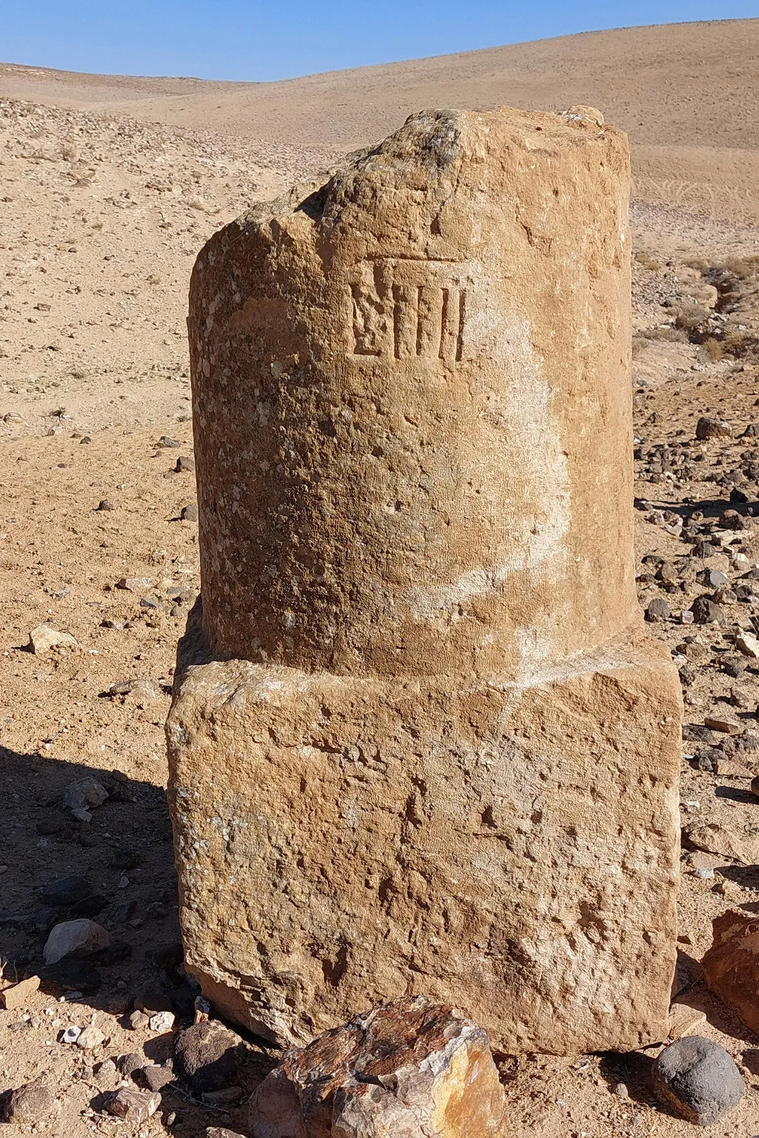 عمود حجري قديم يحمل نقوشًا، يقع في منطقة صحراوية، يشير إلى شبكة الطرق الرومانية القديمة وأهميتها التاريخية.