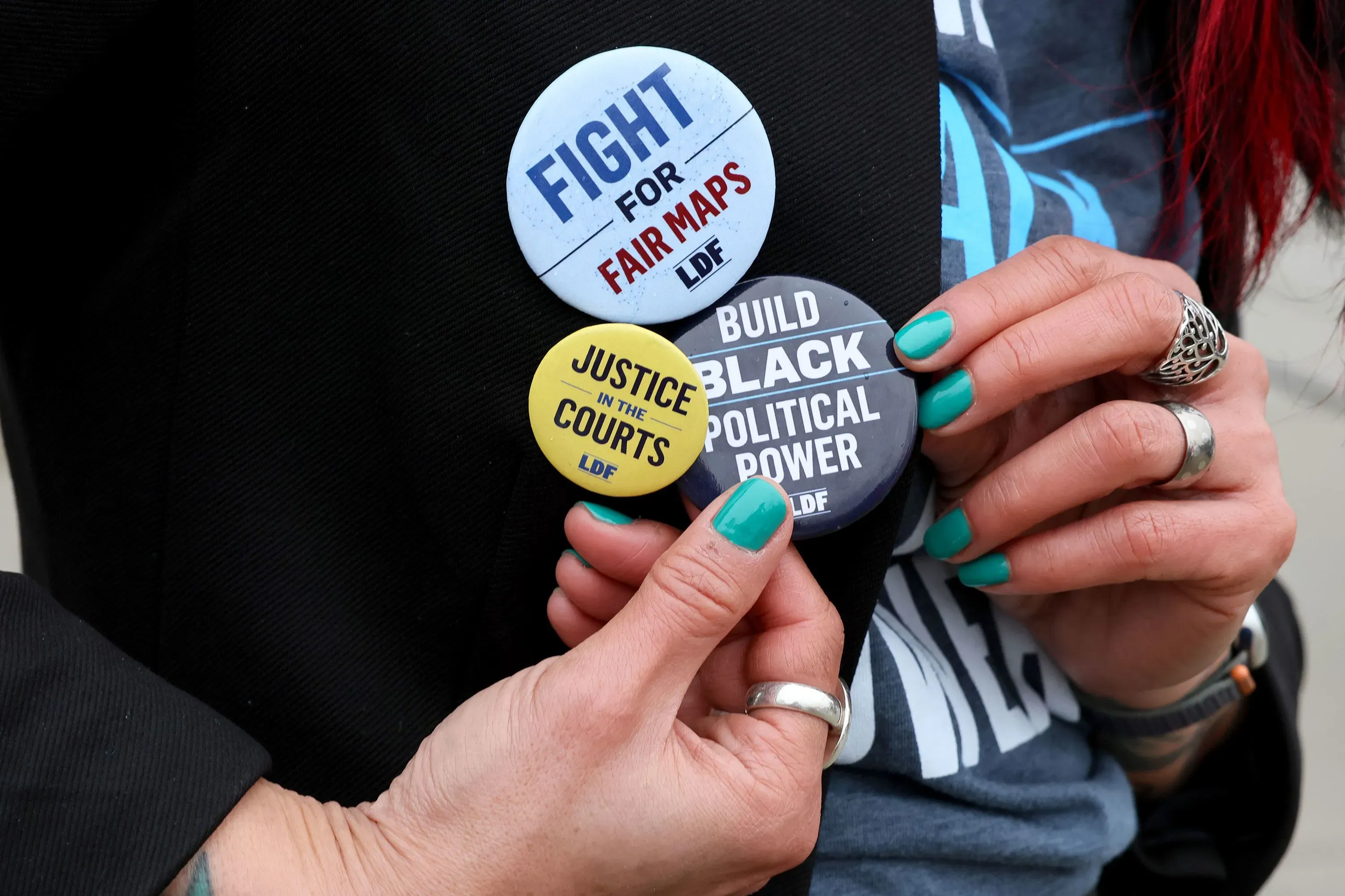 أزرار تحمل شعارات تدعو إلى العدالة السياسية وخرائط انتخابية عادلة، تعكس جهود تعزيز حقوق التصويت للأقليات العرقية.