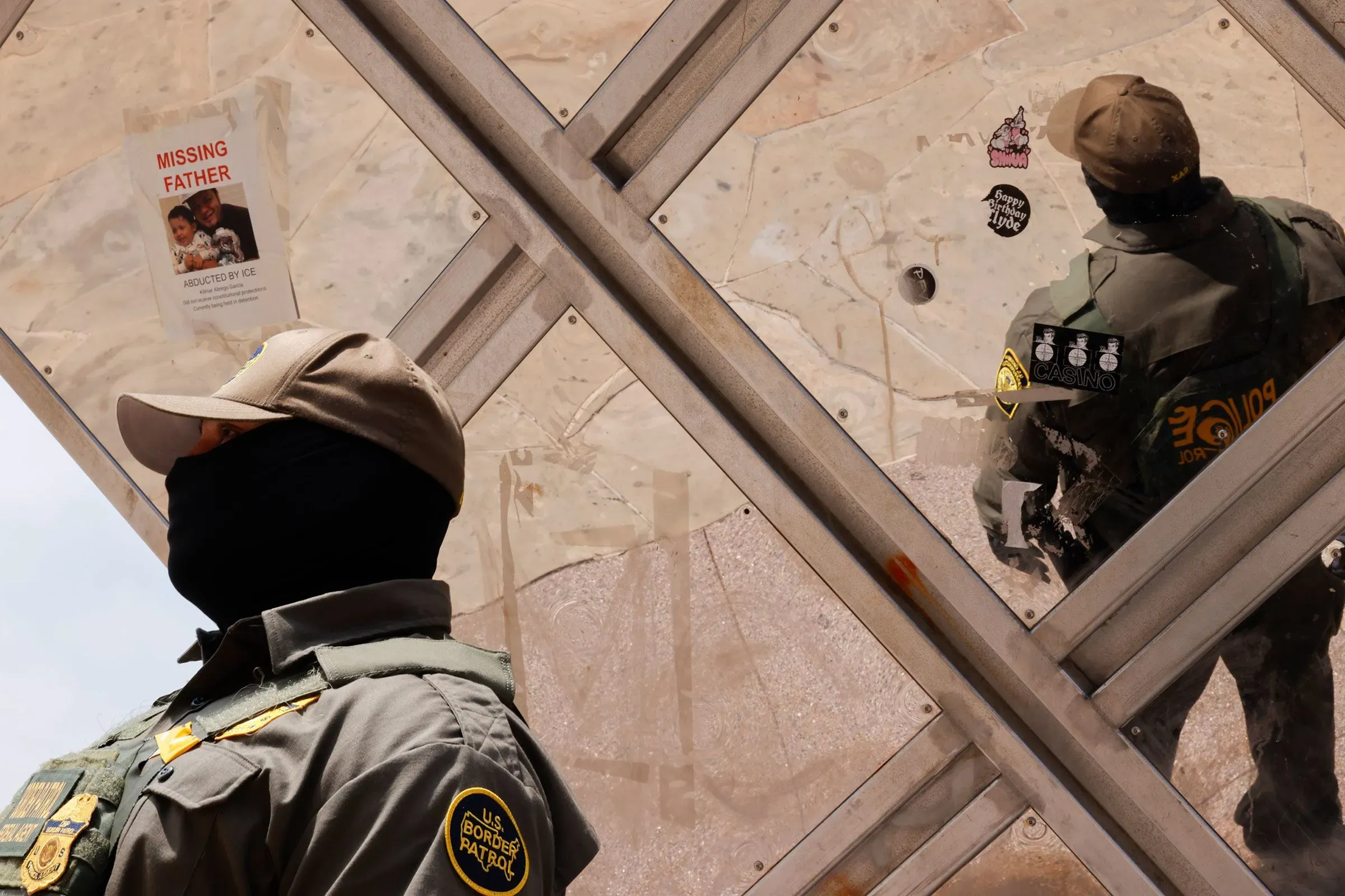 عناصر إنفاذ القانون يرتدون زيهم الرسمي في مكان عام، مع وجود إعلان مفقود في الخلفية، يعكس التوترات حول قضايا الهجرة.