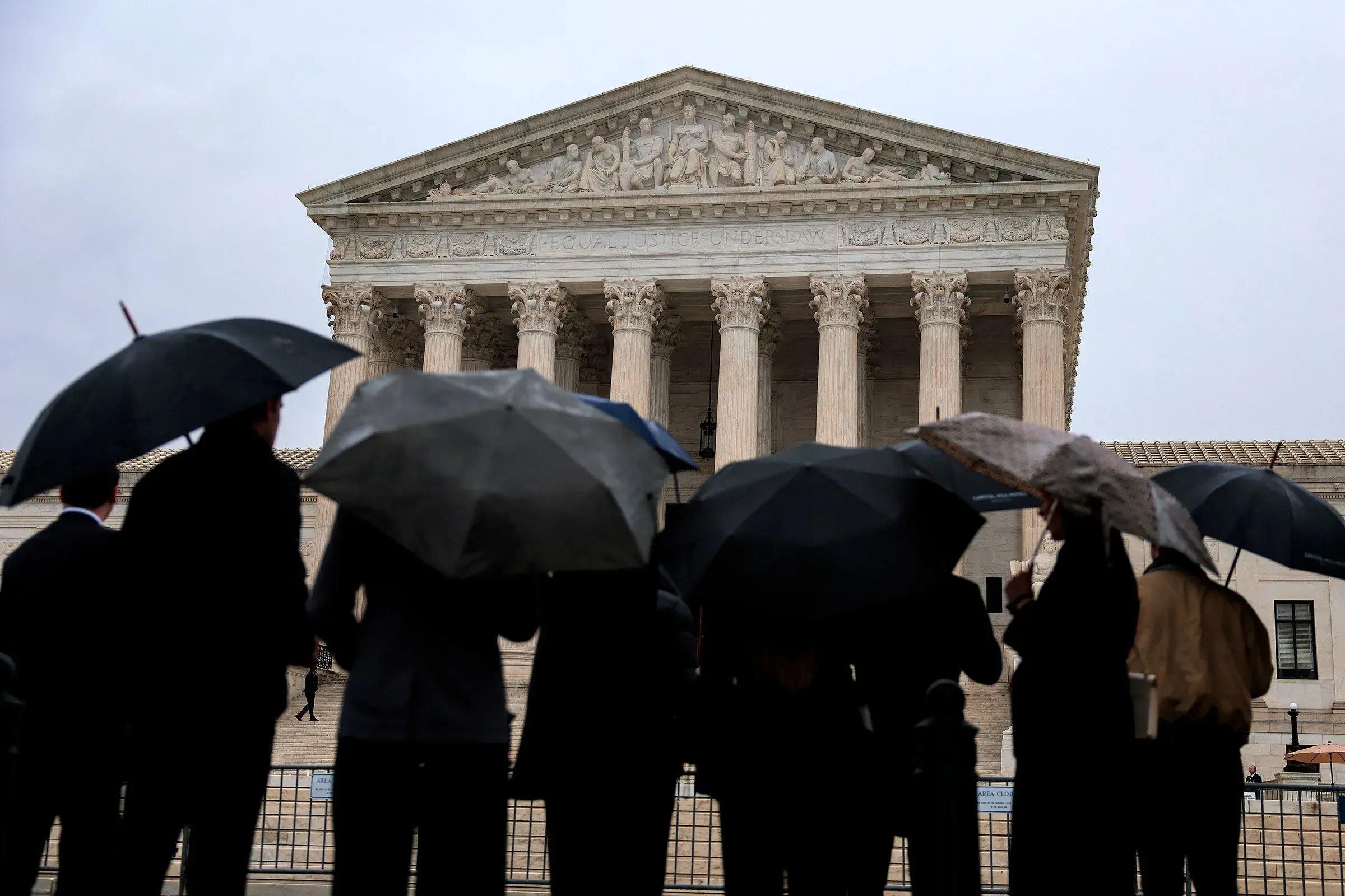 مجموعة من الأشخاص يحملون مظلات أمام مبنى المحكمة العليا الأمريكية، حيث تم الإعلان عن قرار مهم بشأن التعريفات الجمركية.