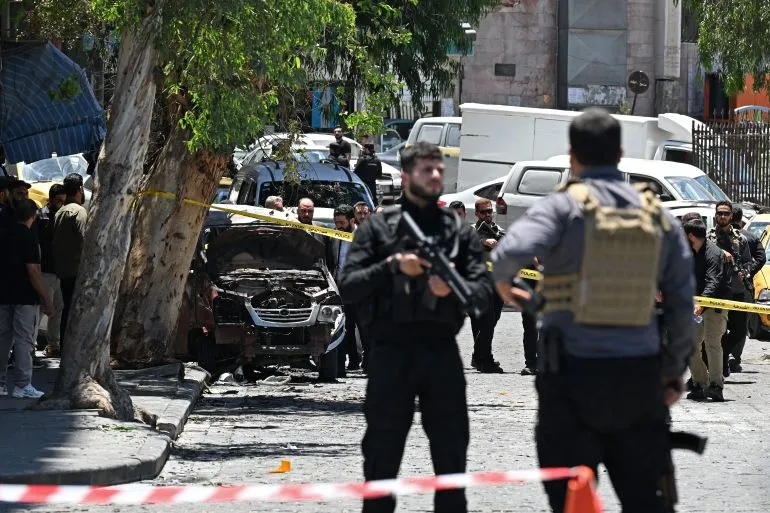 عناصر أمنية سورية تحيط بموقع انفجار سيارة مفخخة في دمشق خلال زيارة الرئيس الفرنسي ماكرون وسط توترات أمنية متصاعدة في سوريا.