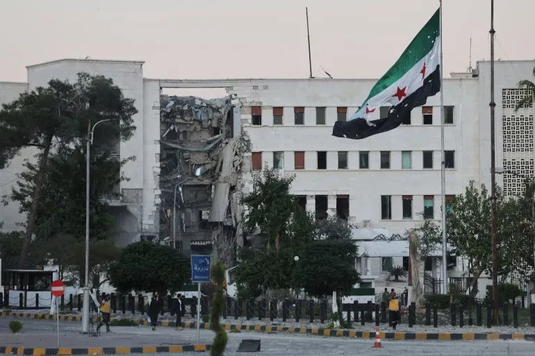 مبنى حكومي في دمشق يظهر آثار الدمار الناتج عن الضربات الإسرائيلية، مع العلم السوري يرفرف في الخلفية.