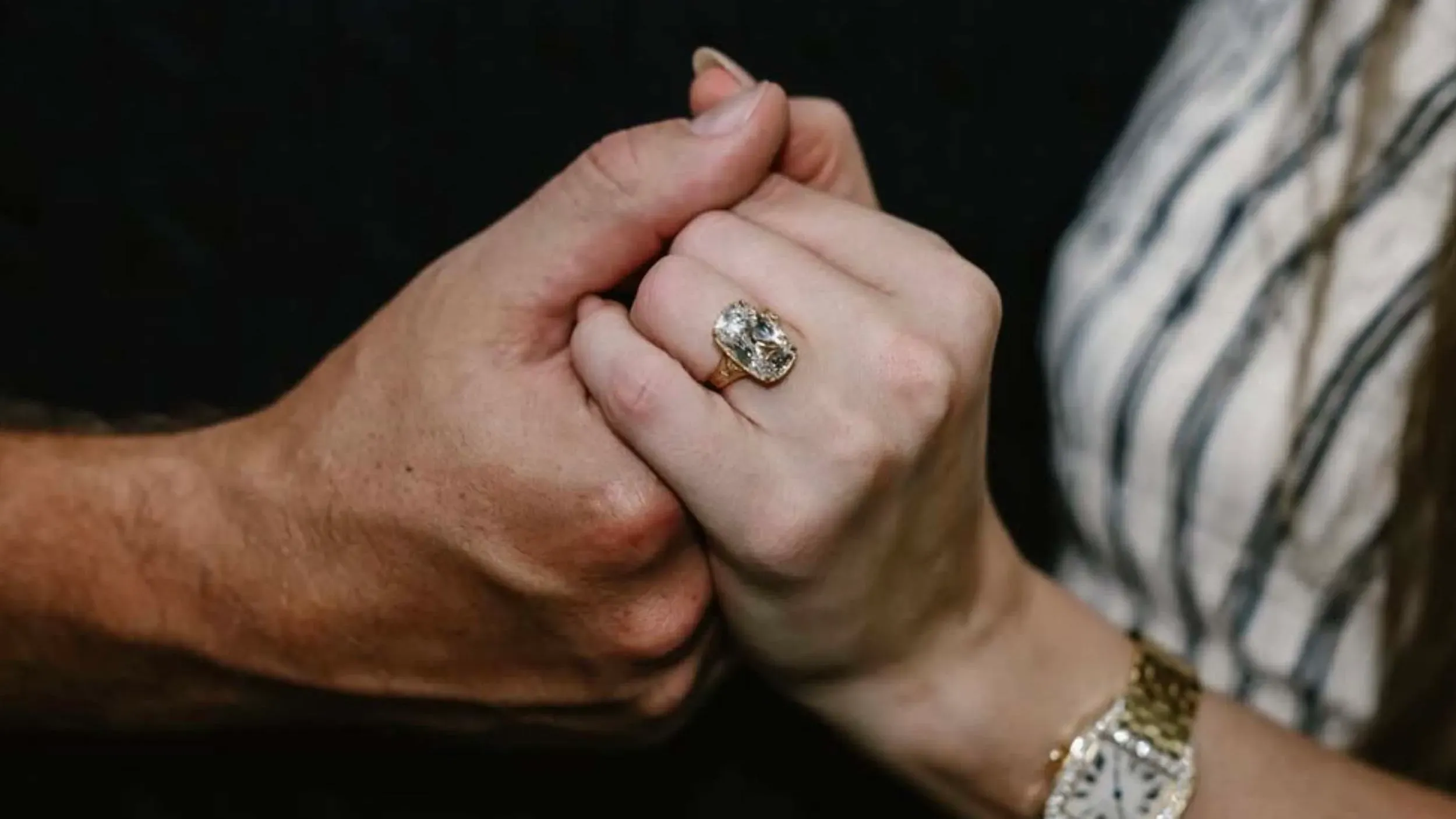 خاتم خطوبة ماسي عتيق بحجر كبير يزين إصبع امرأة، بينما تمسك يد رجل بيدها، مما يعكس لحظة رومانسية.