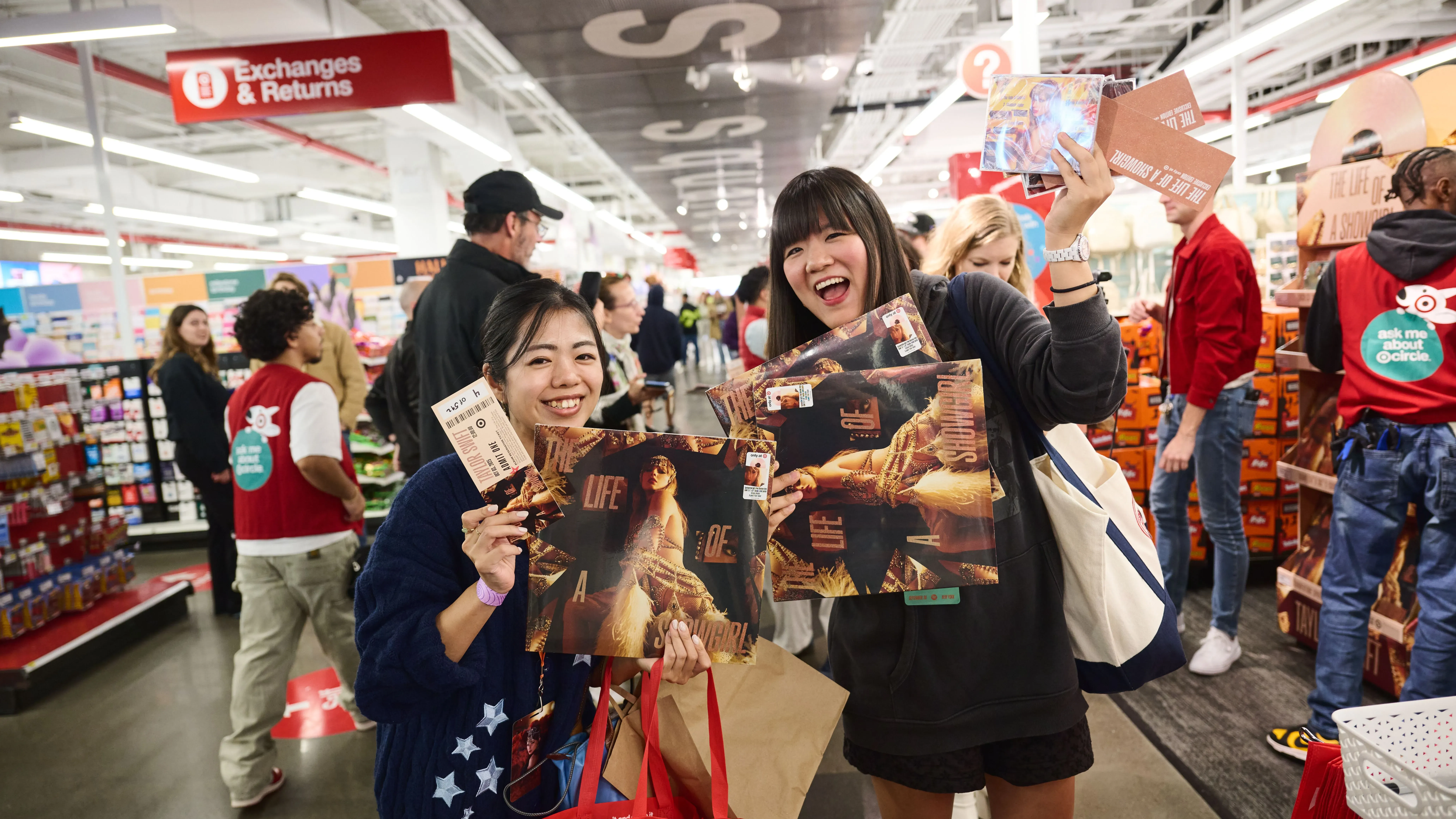 معجبون بتايلور سويفت يحتفلون بإطلاق ألبومها الجديد "The Life of a Showgirl" في متجر، يحملون الألبوم والتذاكر ويبتسمون.