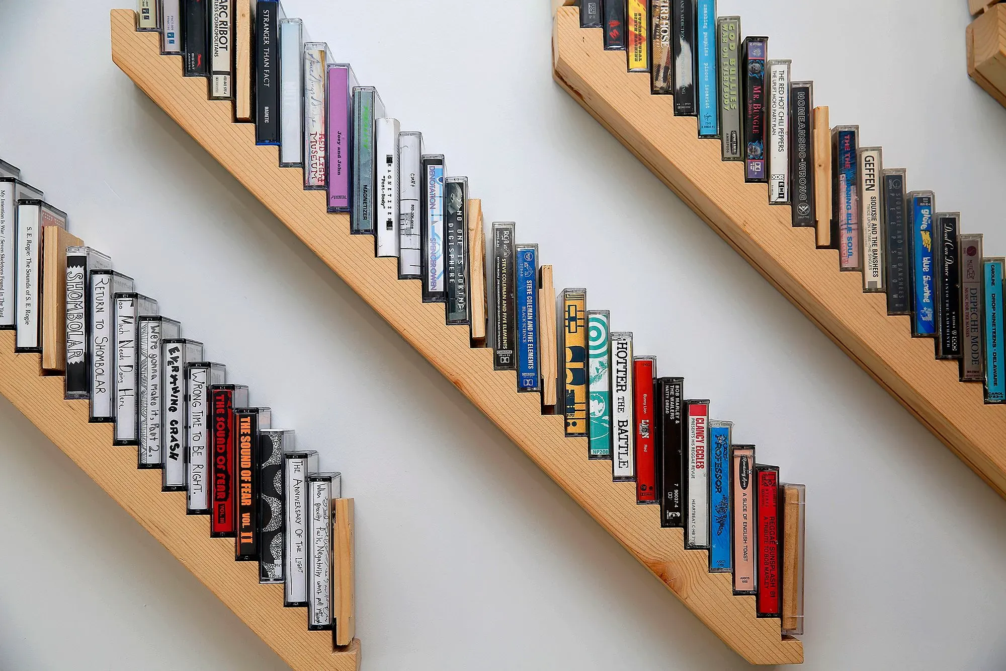 رفوف خشبية تحمل مجموعة من أشرطة الكاسيت الملونة، تعكس عودة شعبية الكاسيت كوسيلة للاستماع للموسيقى في العصر الحديث.